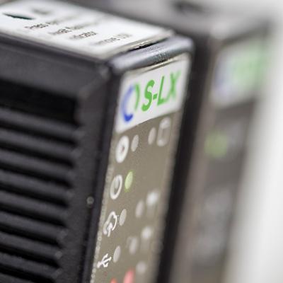 Close-up of electronic device with "S-LX" label, showing various buttons and indicators. The focus is on the corner of the device.