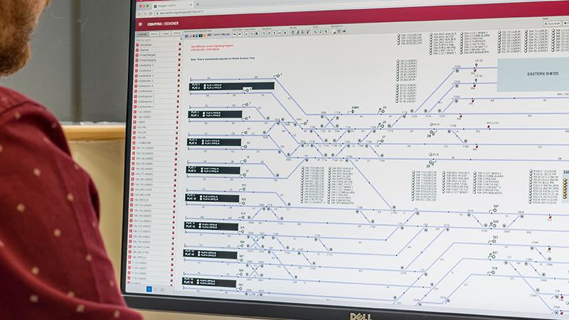 Person viewing a computer screen displaying a complex network diagram with nodes, lines, and text details in a software interface.