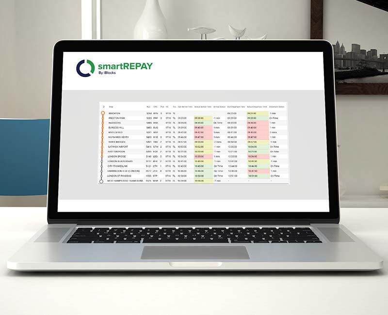 Laptop displaying a financial spreadsheet with color-coded data under the "smartREPAY" logo, on a desk with a vase and framed cityscape.
