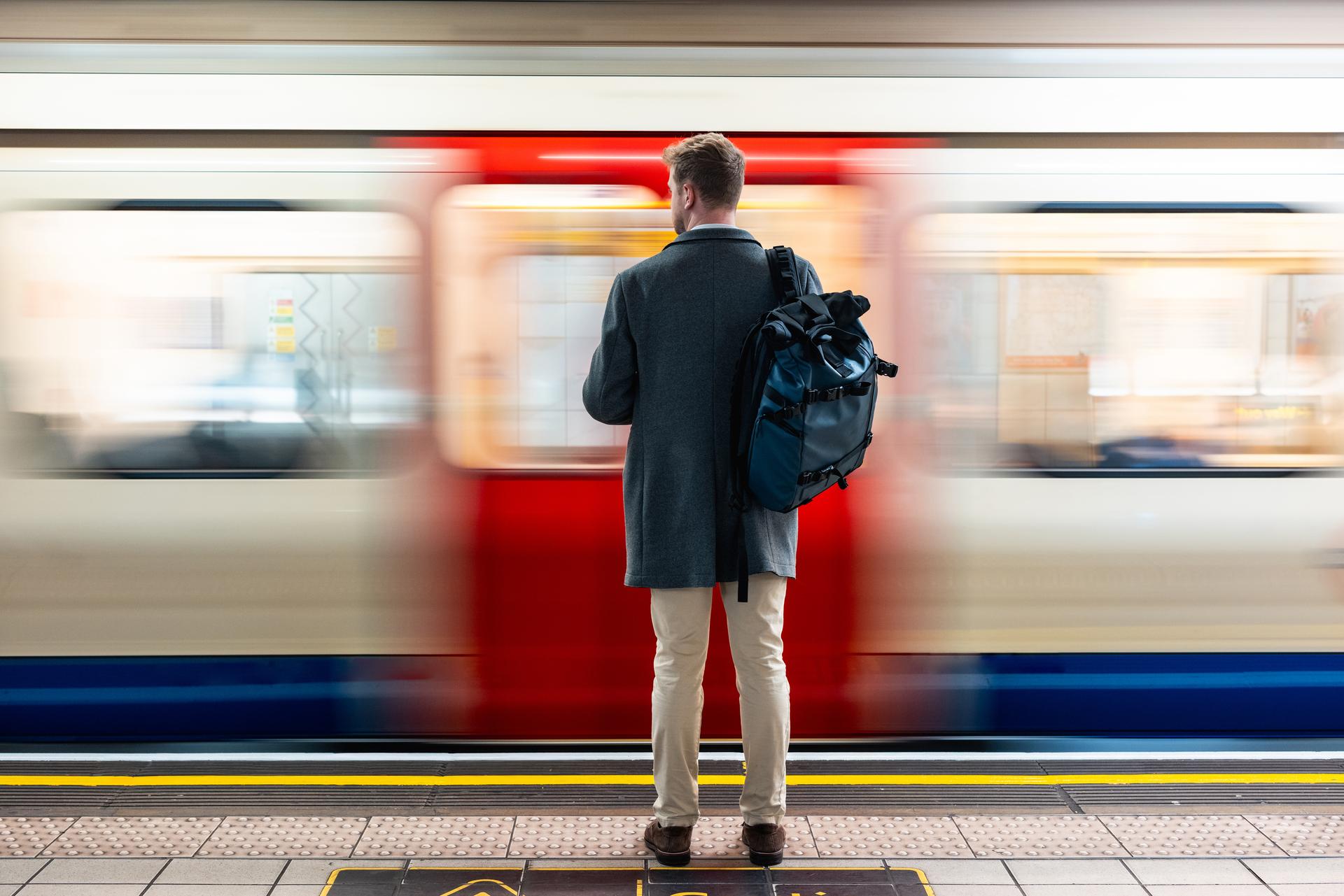 Man waits on a platform as a train blurs by in front of him