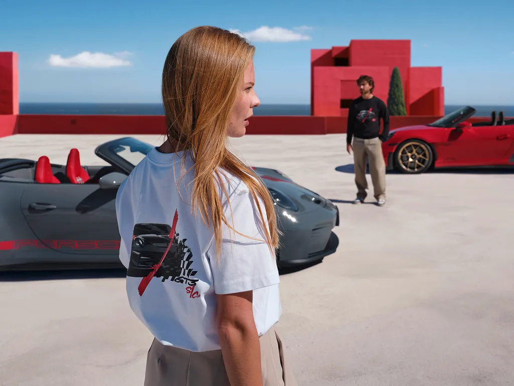 Mann und eine Frau, die Kleidung aus der Porsche 911 GT3 S/C Lifestyle-Kollektion tragen und vor zwei Porsche 911 GT3 S/C stehen.