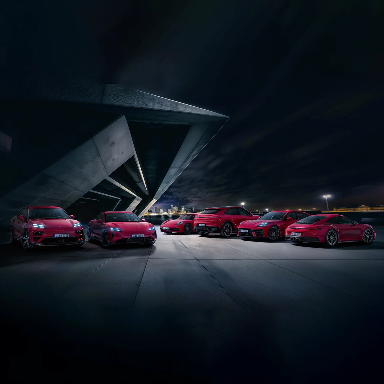 Several red Porsche cars are parked in front of a large building in the evening.