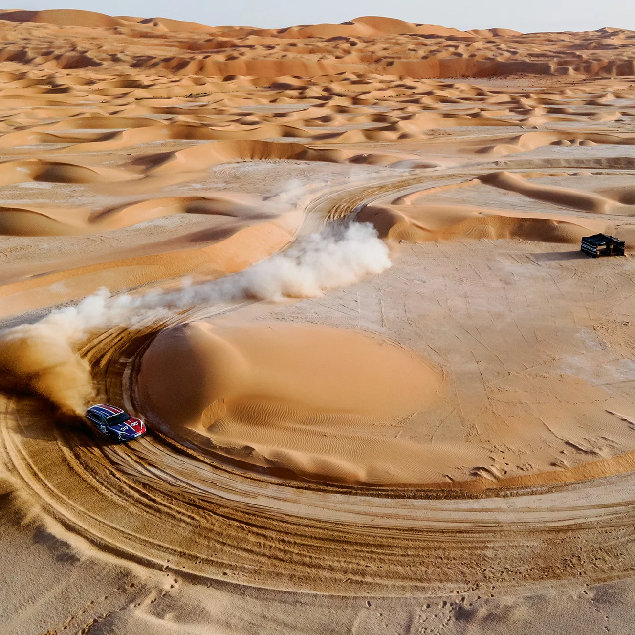 Um carro de corrida circula em rápido movimento por uma curva num deserto arenoso.