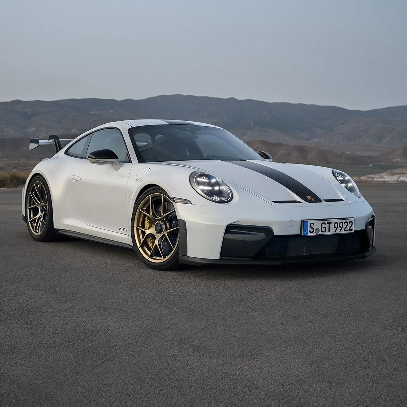 Une voiture de sport Porsche blanche stationnée sur une route ouverte avec un paysage vallonné en arrière-plan.