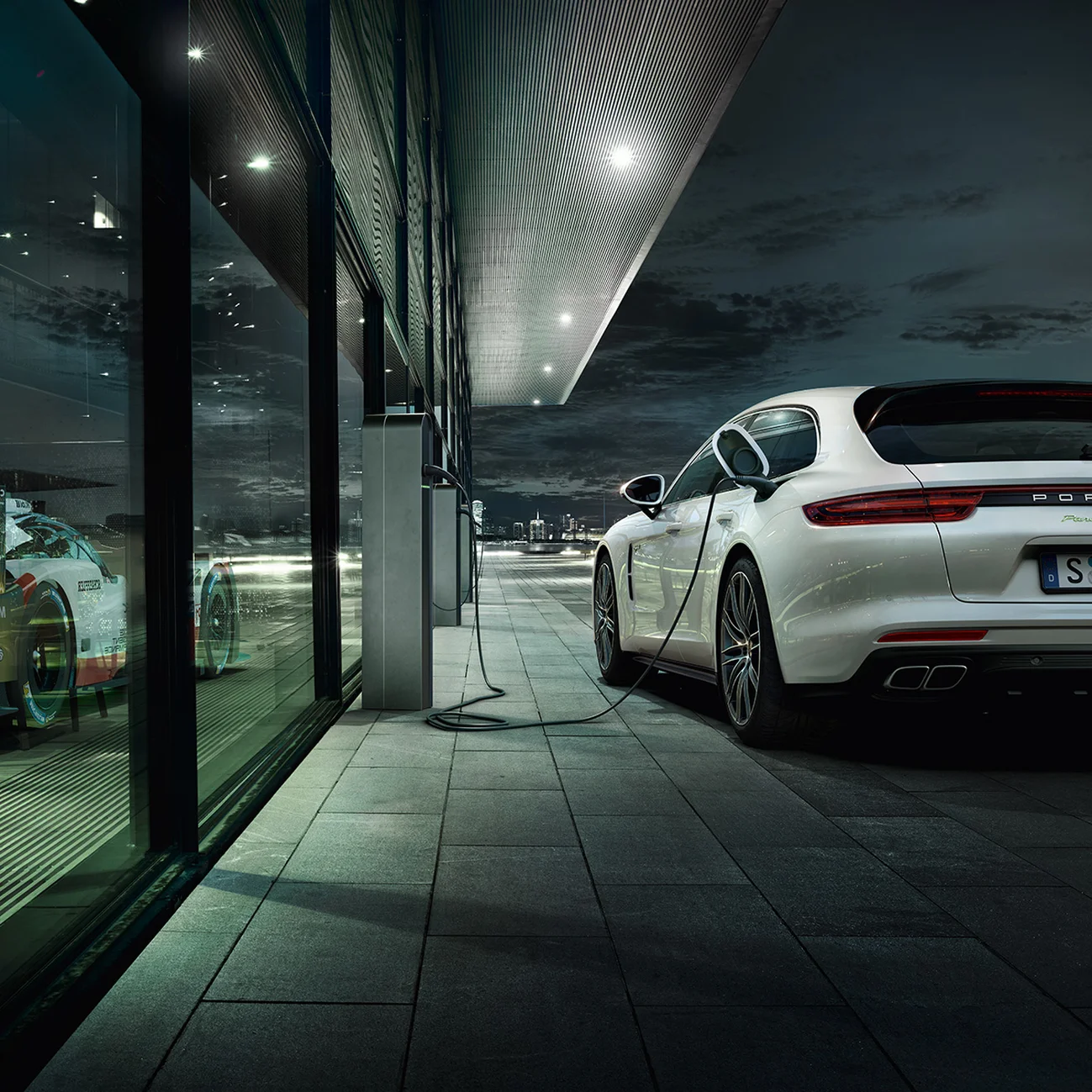 A white Porsche parked outside and charging next to a building.