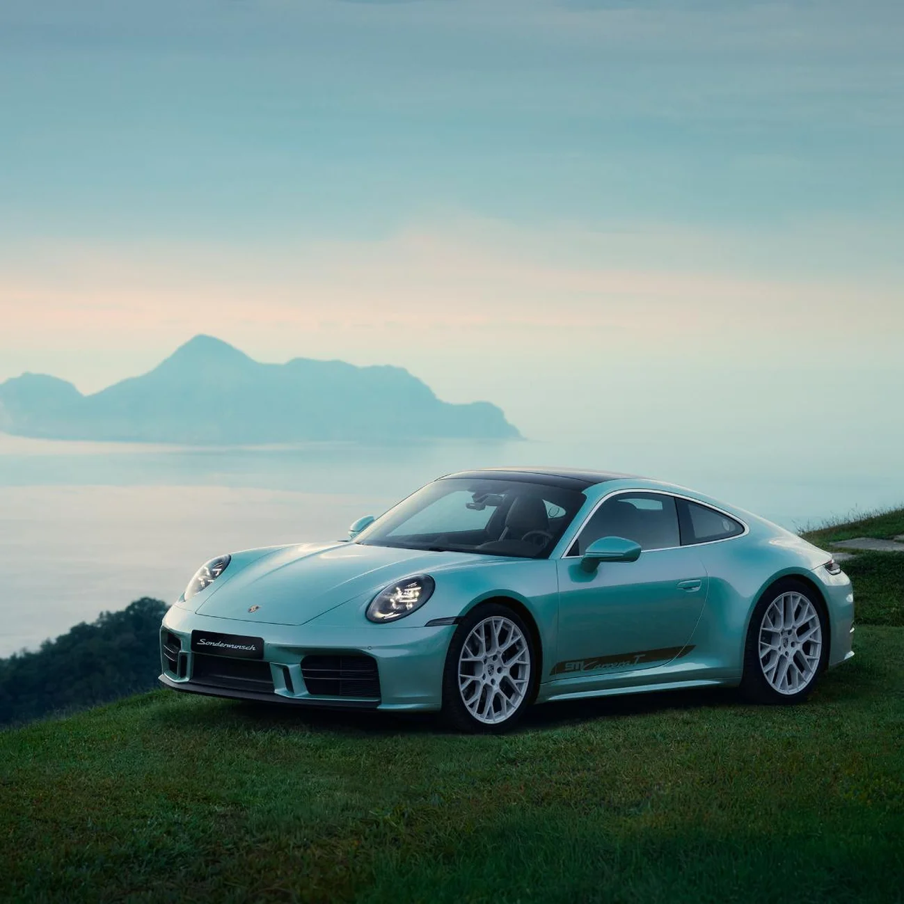 A blue 911 Carrera T Formosa on the grass in front of the coastline.