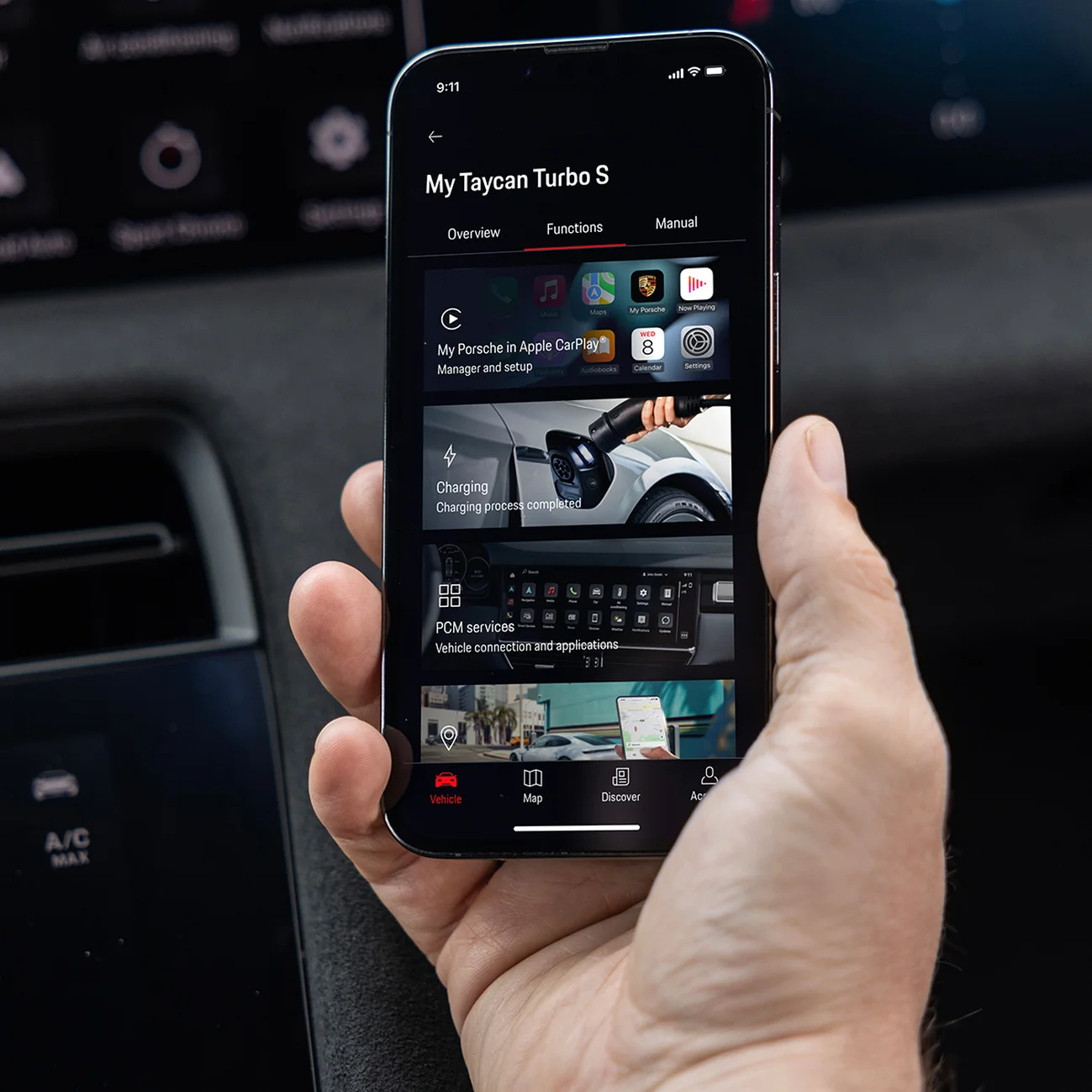 Smartphone dans une main affichant les options de service de l'application MyPorsche, avec l'intérieur d'une Porsche Taycan Turbo S subtilement visible.
