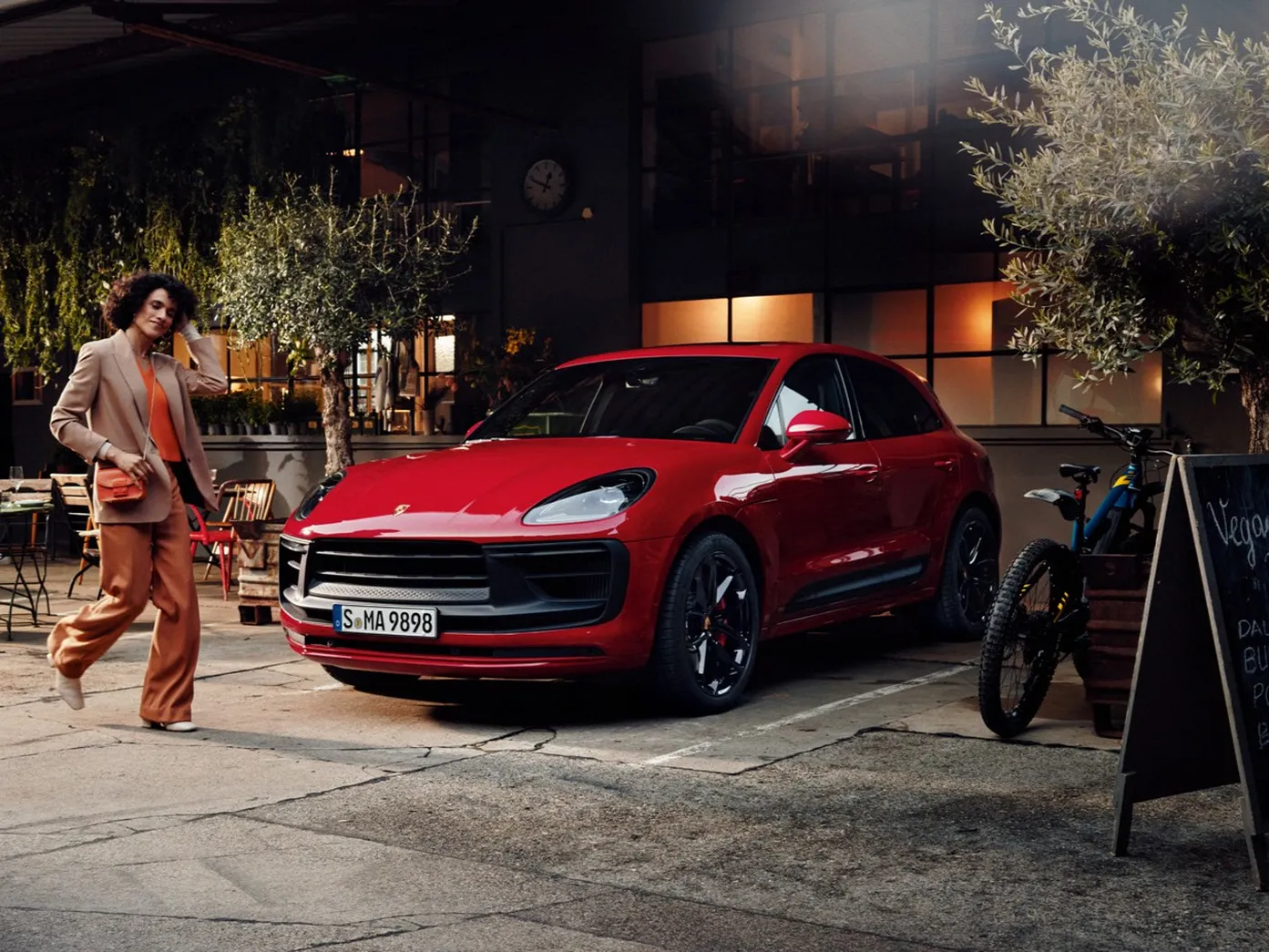 A red SUV is parked in front of a stylish café. A person in a beige suit walks by.