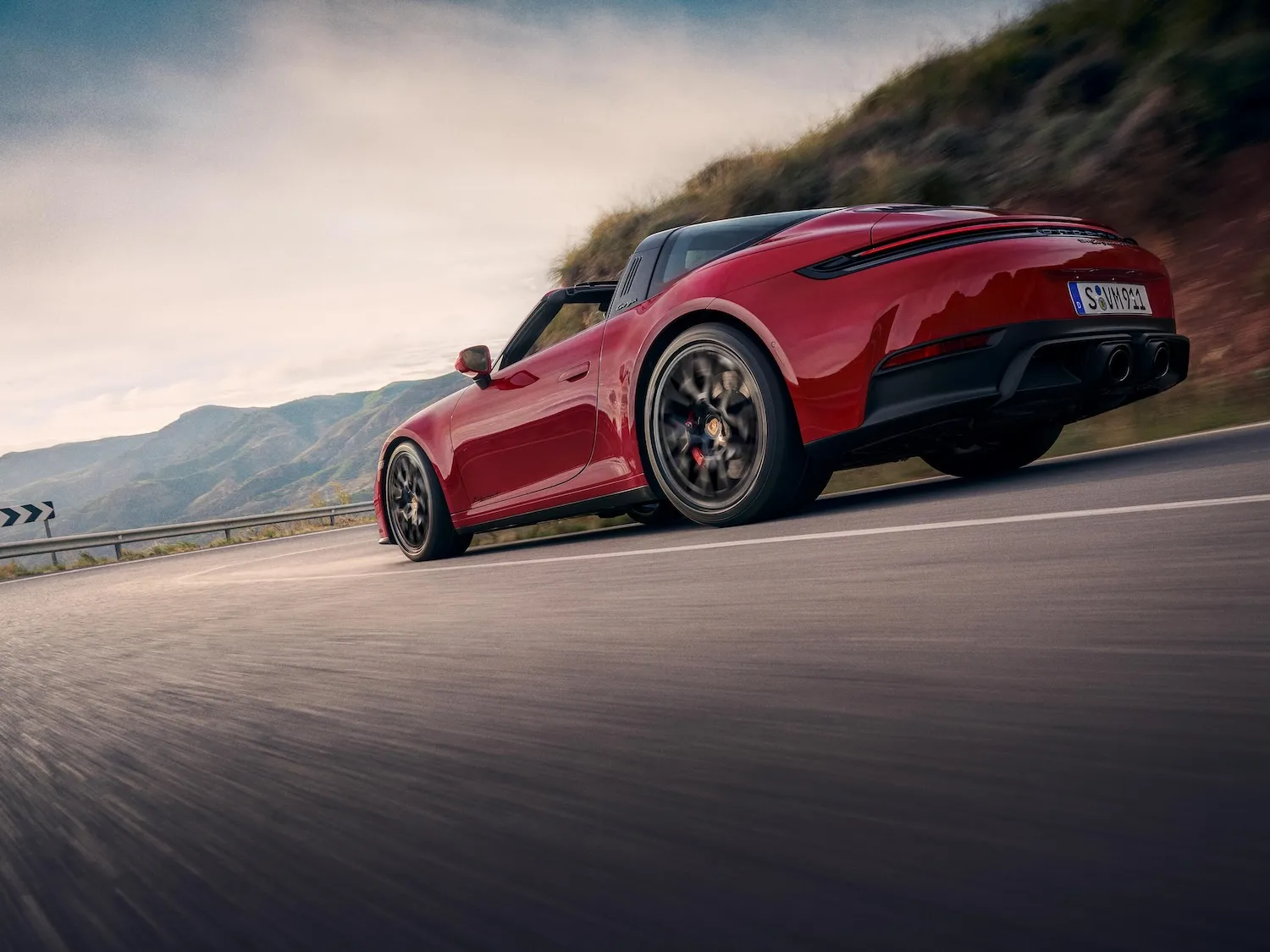 Side shot of a Carmine Red 911 Targa 4 GTS driving on a street through the mountains.
