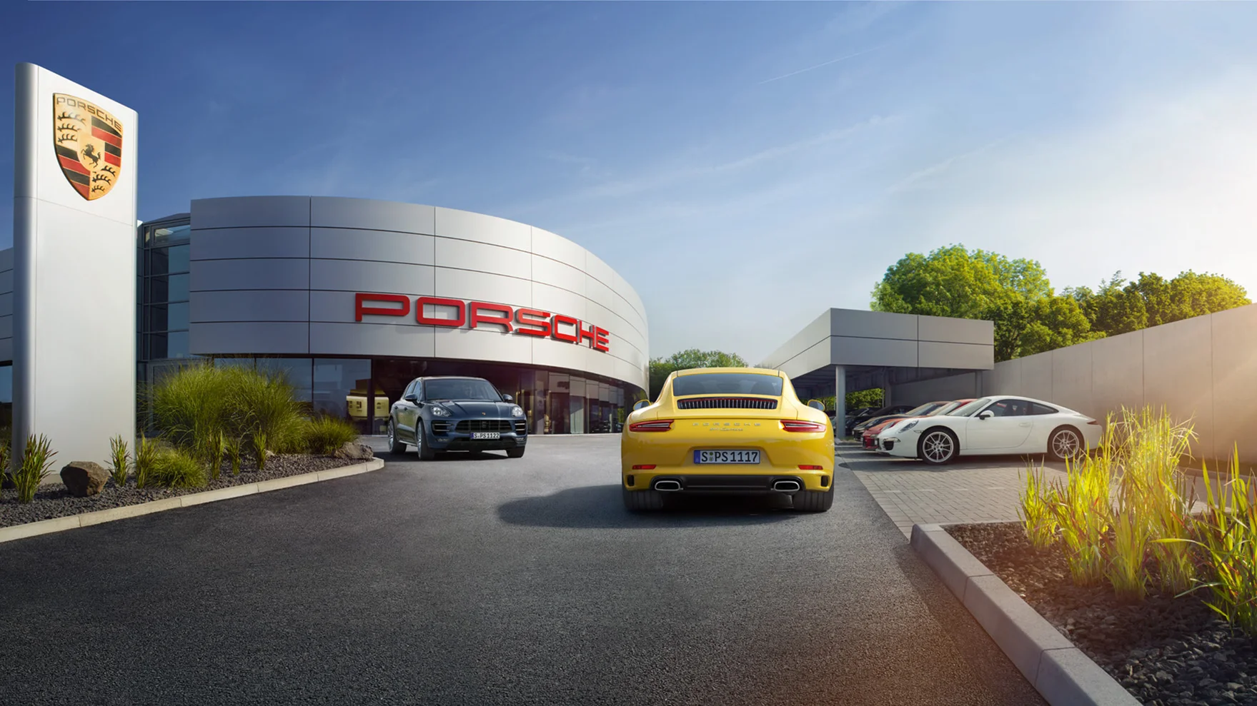 Un centre Porsche à l'arrière-plan et plusieurs voitures Porsche dans les environs.