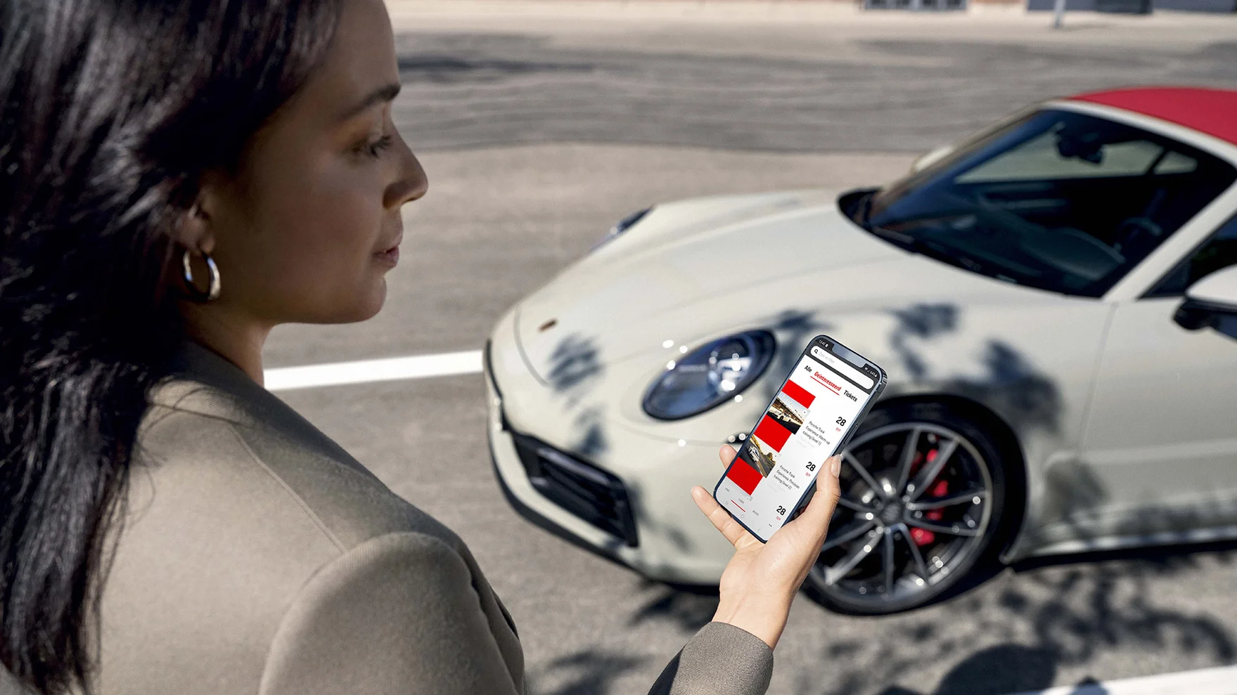 Een vrouw staat voor een Porsche met een mobiel in haar hand, hierop is de Porsche 24 app te zien.