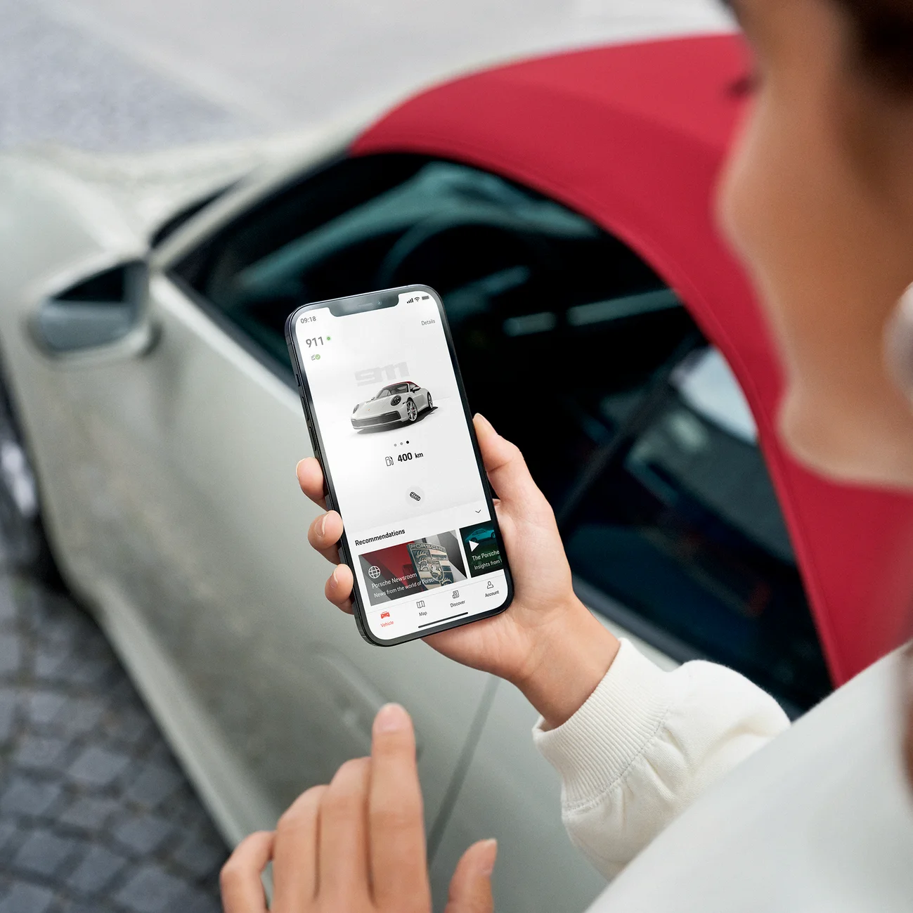 A woman using the My Porsche app while standing next to a parked 911 Carrera S Cabriolet.