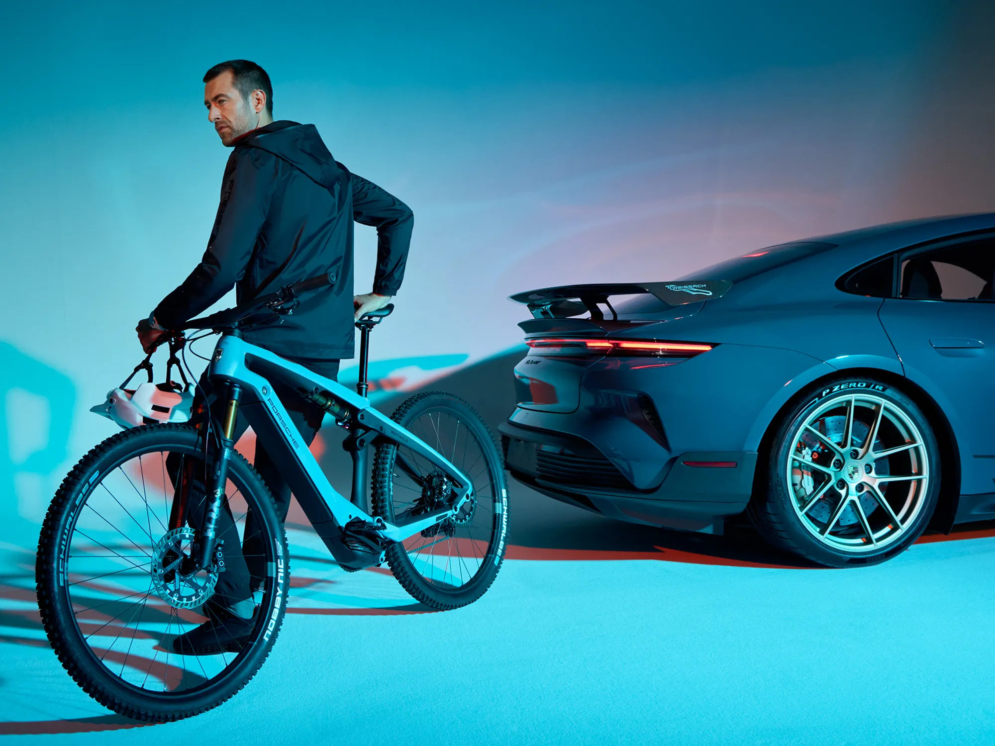 Un hombre apoyado sobre una Porsche e-bike con un Porsche deportivo de fondo.