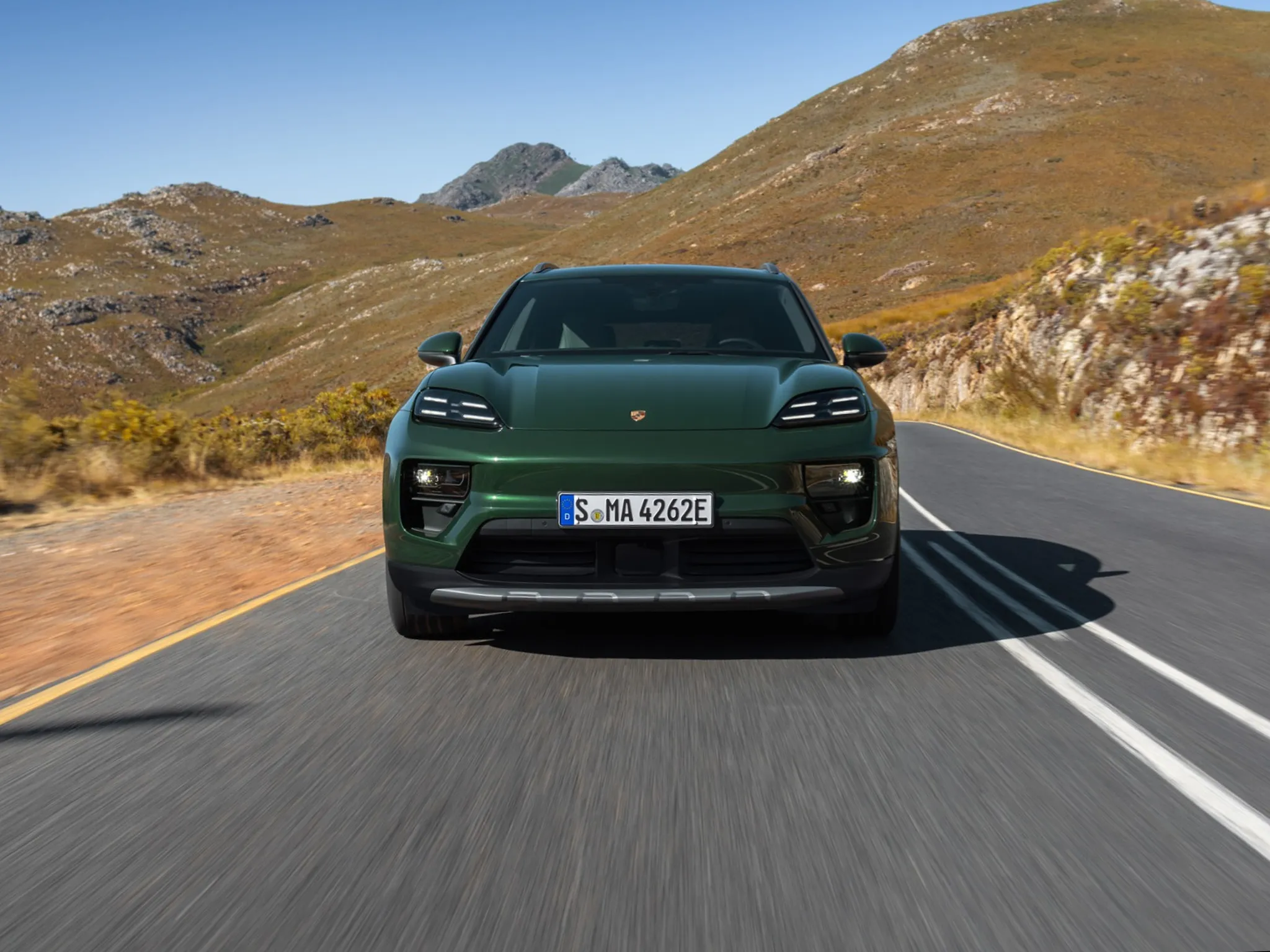Rear shot of an Oak Green Metallic Neo Macan 4S standing in front of a lake with the mountains in the background.