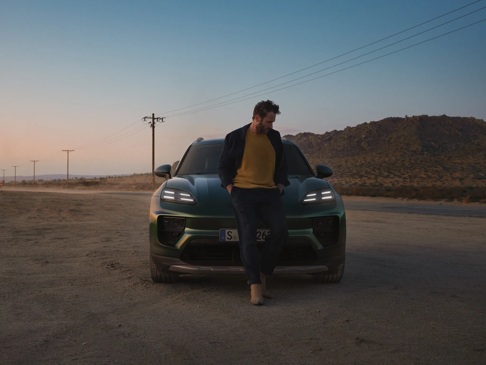 A man standing in front of a green Porsche Macan in the desert. 