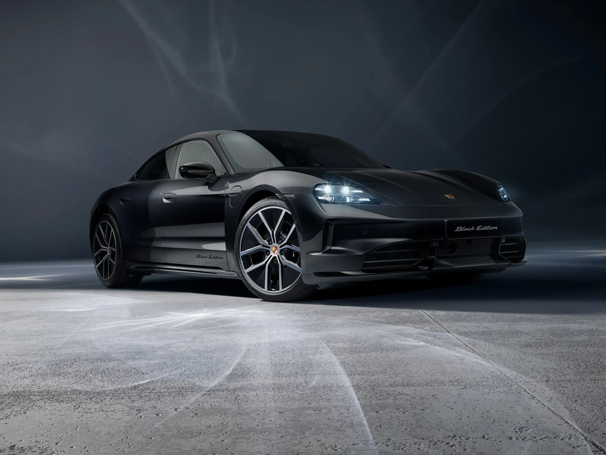 Front shot of Black Taycan 4S parked on grey concrete and a dark grey background.