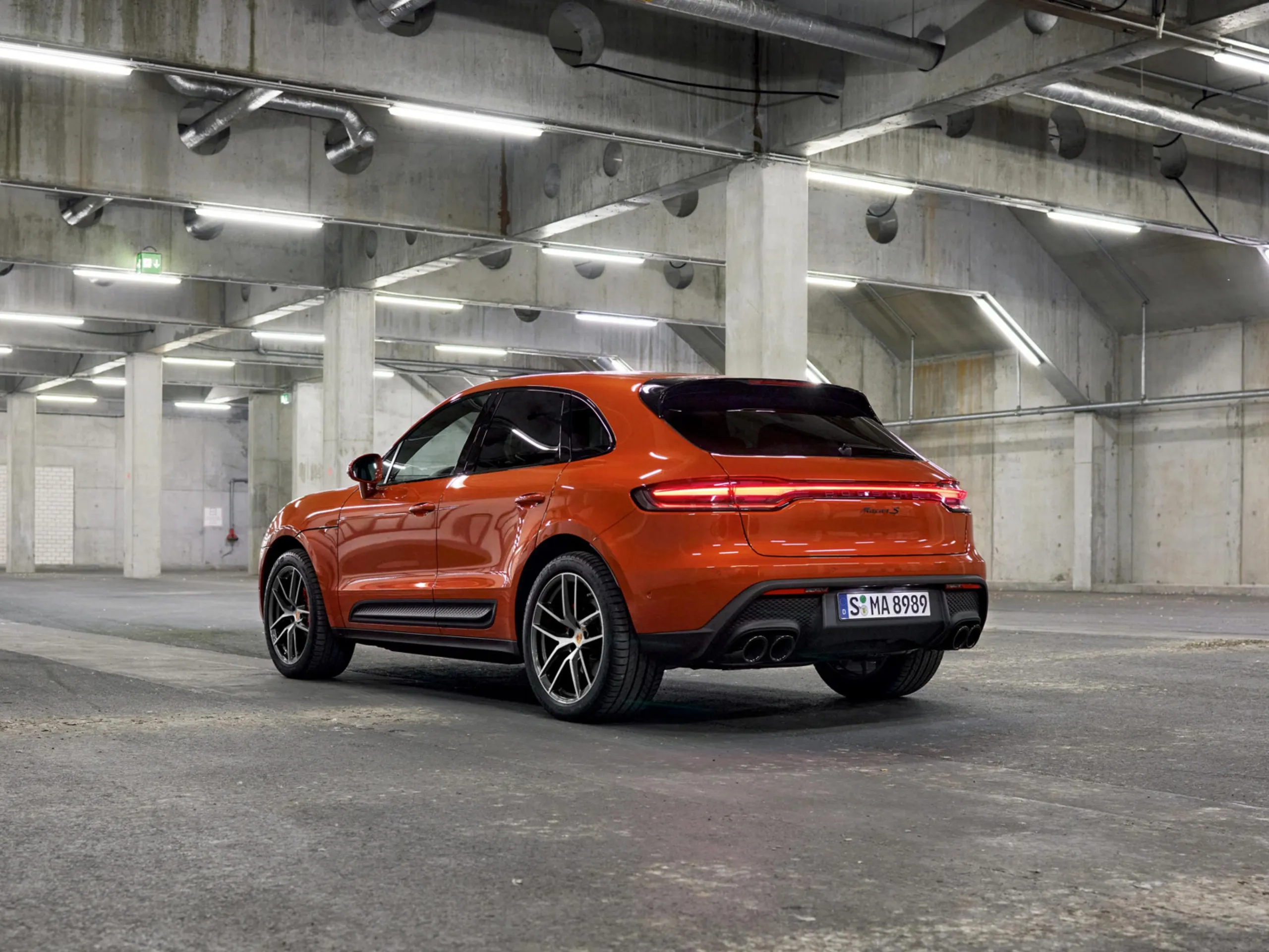A rear shot of an orange Porsche Macan in an underground parking structure.