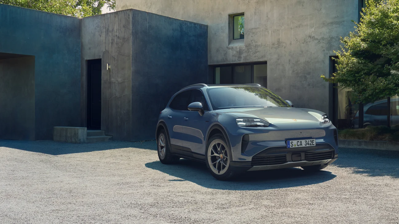A pale blue metallic Cayenne S Electric parked in front of a modern concrete house.
