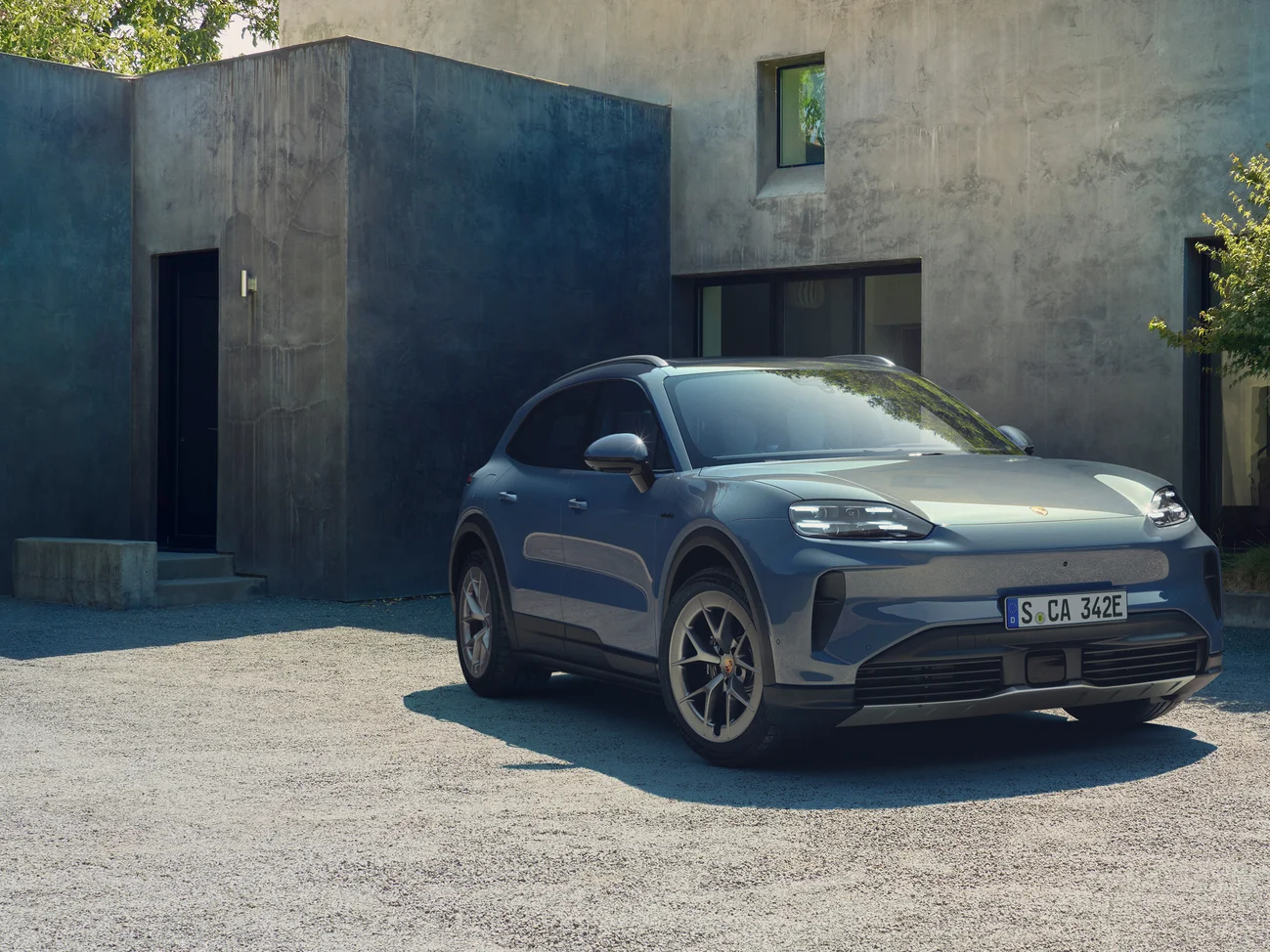 A pale blue metallic Cayenne S Electric parked in front of a modern concrete house.