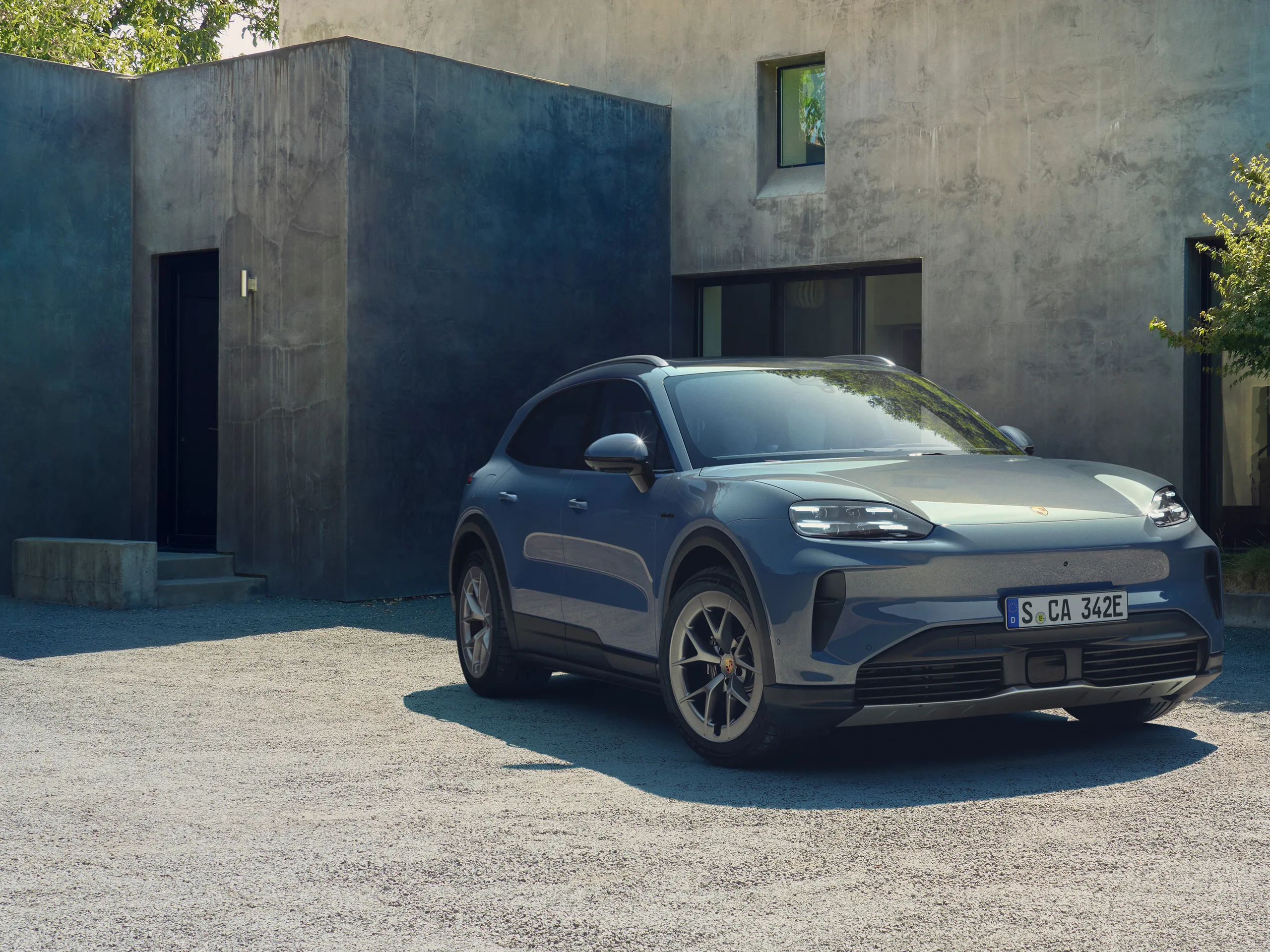 A pale blue metallic Cayenne S Electric parked in front of a modern concrete house.
