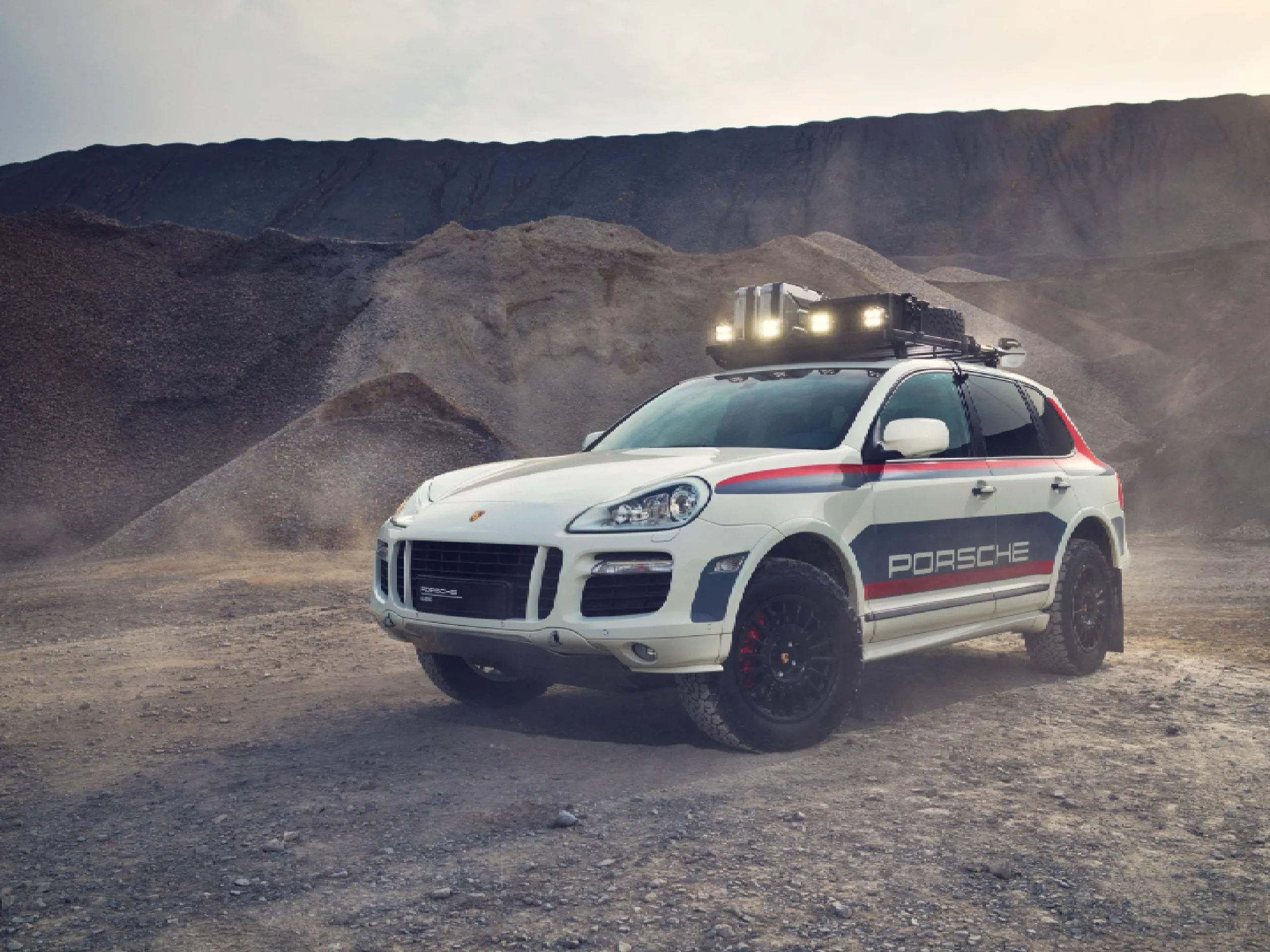 A modified classic Porsche Cayenne parked on a rocky mountain road.