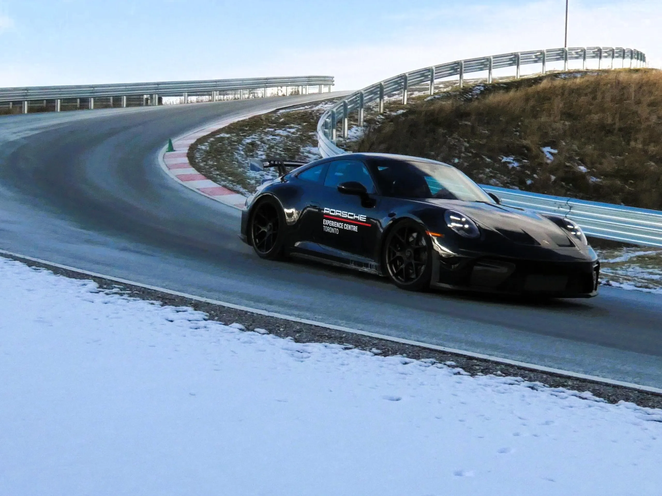 A black Porsche 911 GT3 driving on a circuit with light snow in the background.