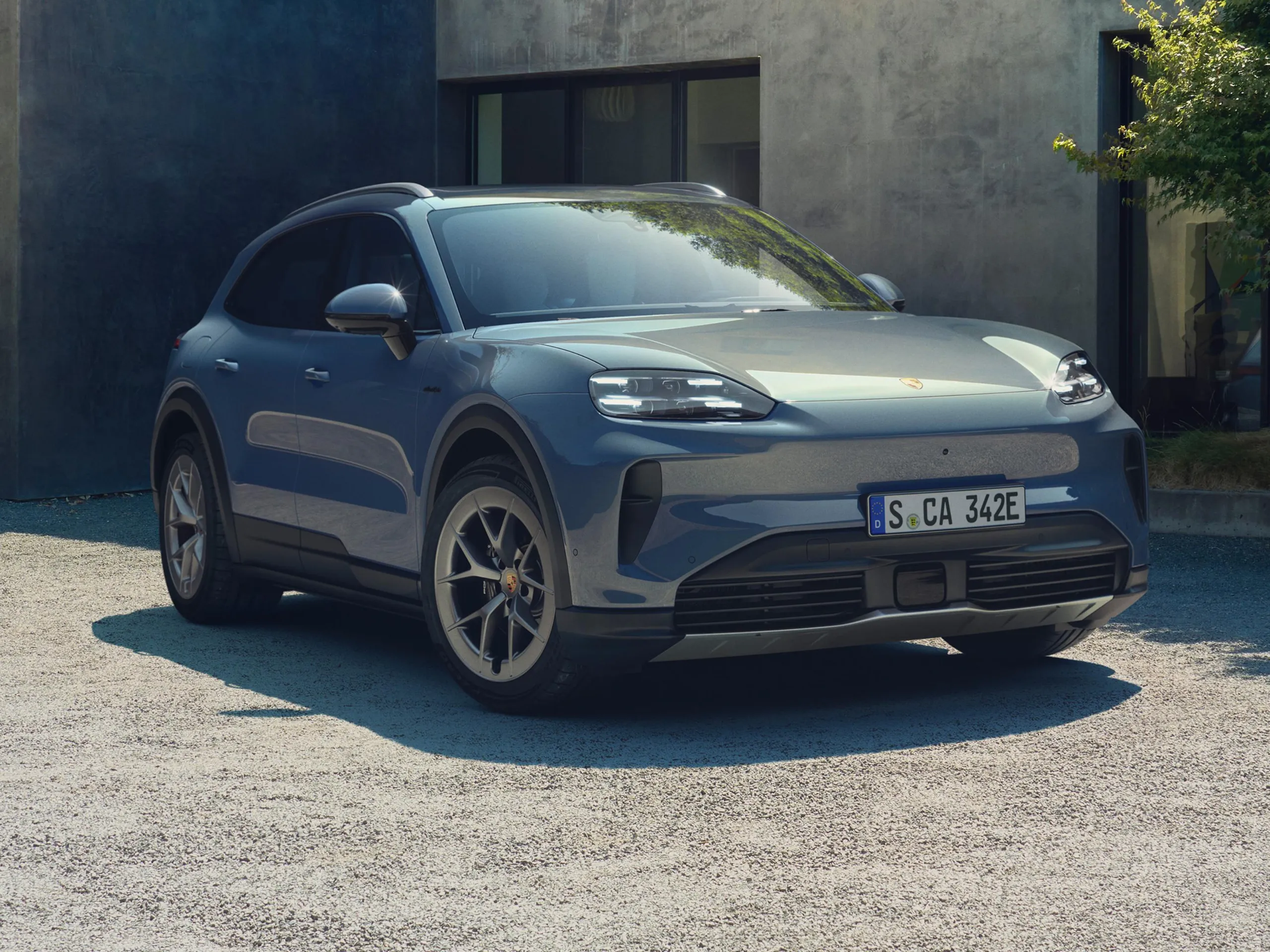 A pale blue metallic Cayenne S Electric parked in front of a modern concrete house.