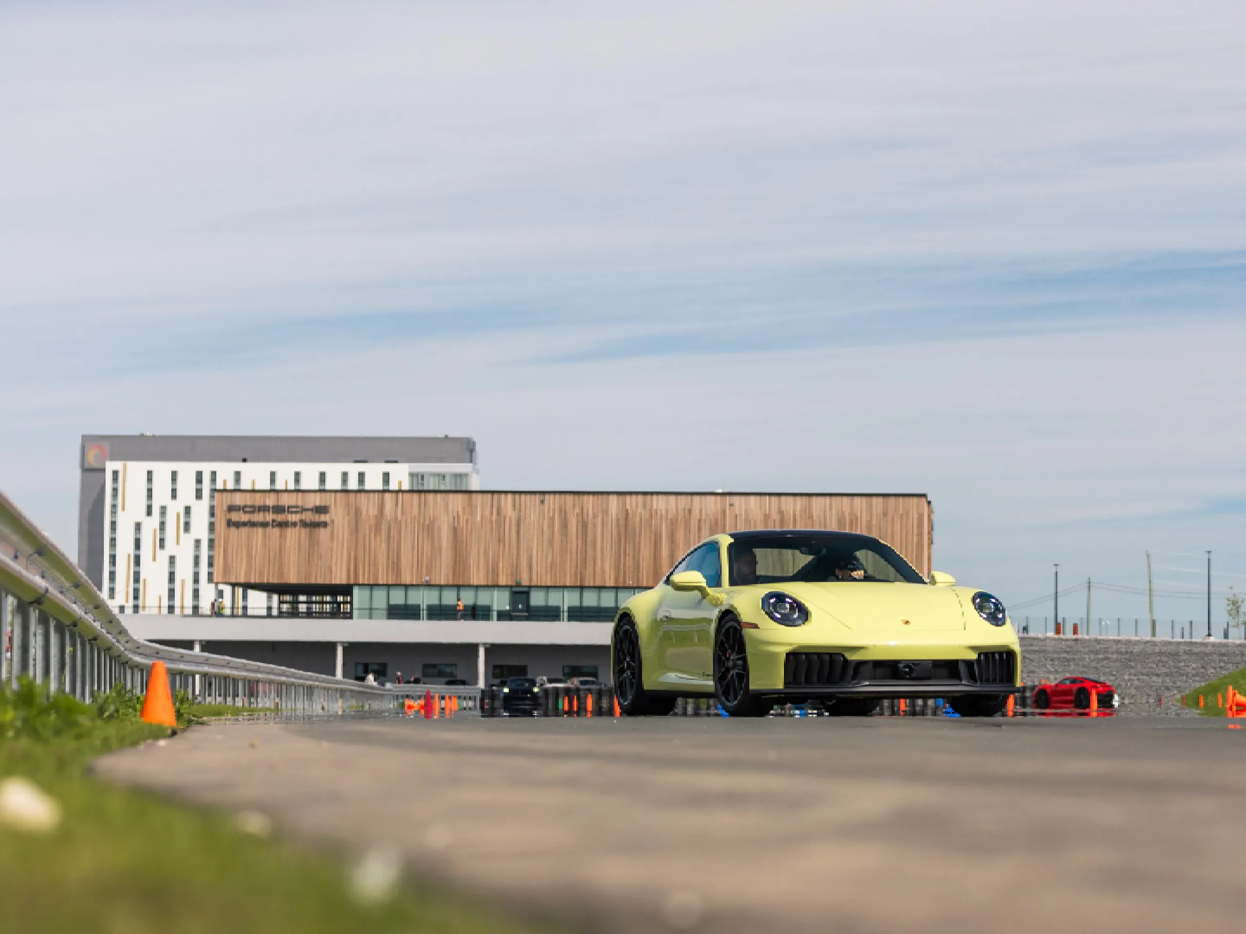 A yellow Porsche 911 driving down a track with a modern building in the background.