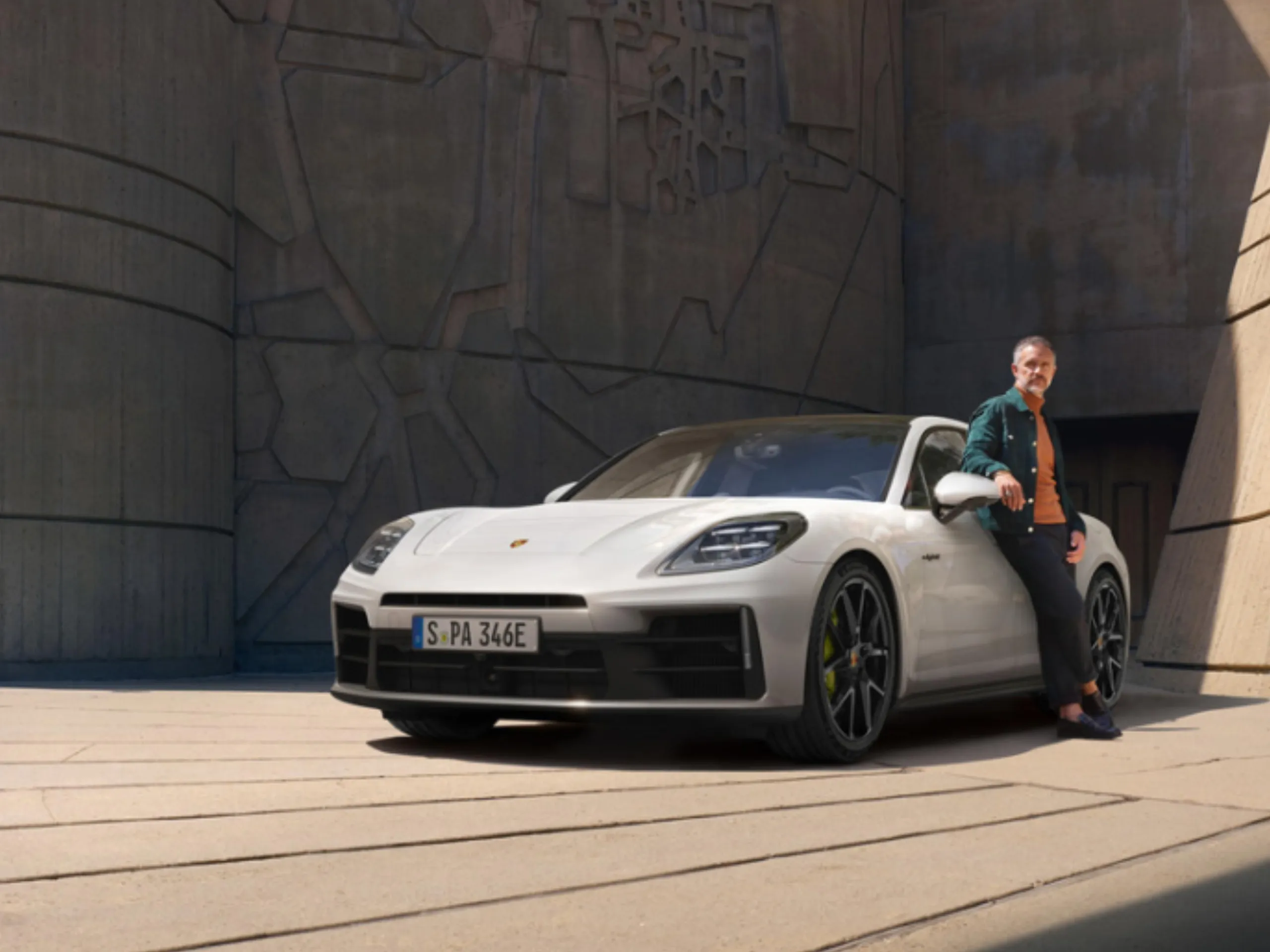 Shot of a white Panamera 4 E-Hybrid standing in front of a modern building with a man standing next to it.