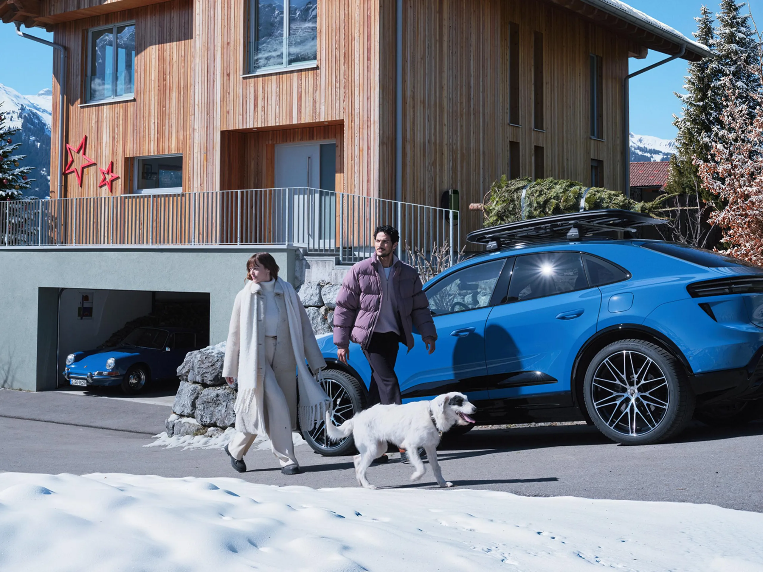 A little girl and her father near a Christmas tree and 2 Porsche cars.