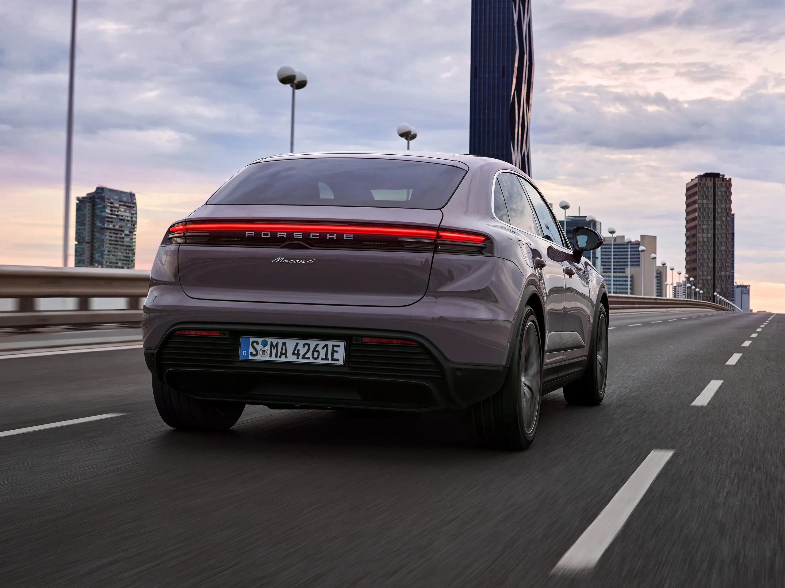 A provence Macan 4 driving on a bridge with a city skyline in the background.