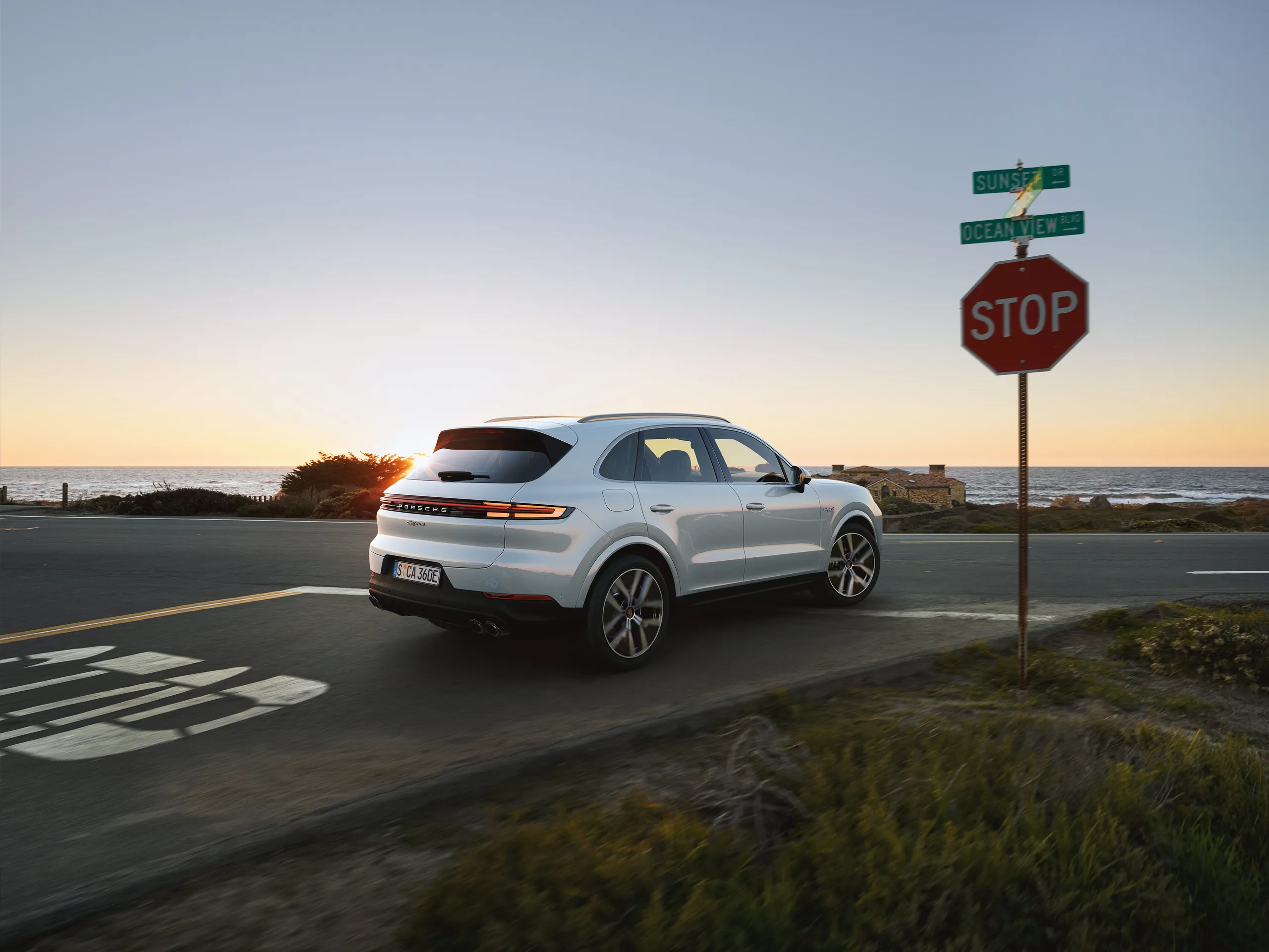 A white Porsche Cayenne stopped at a stop sign waiting to turn right.