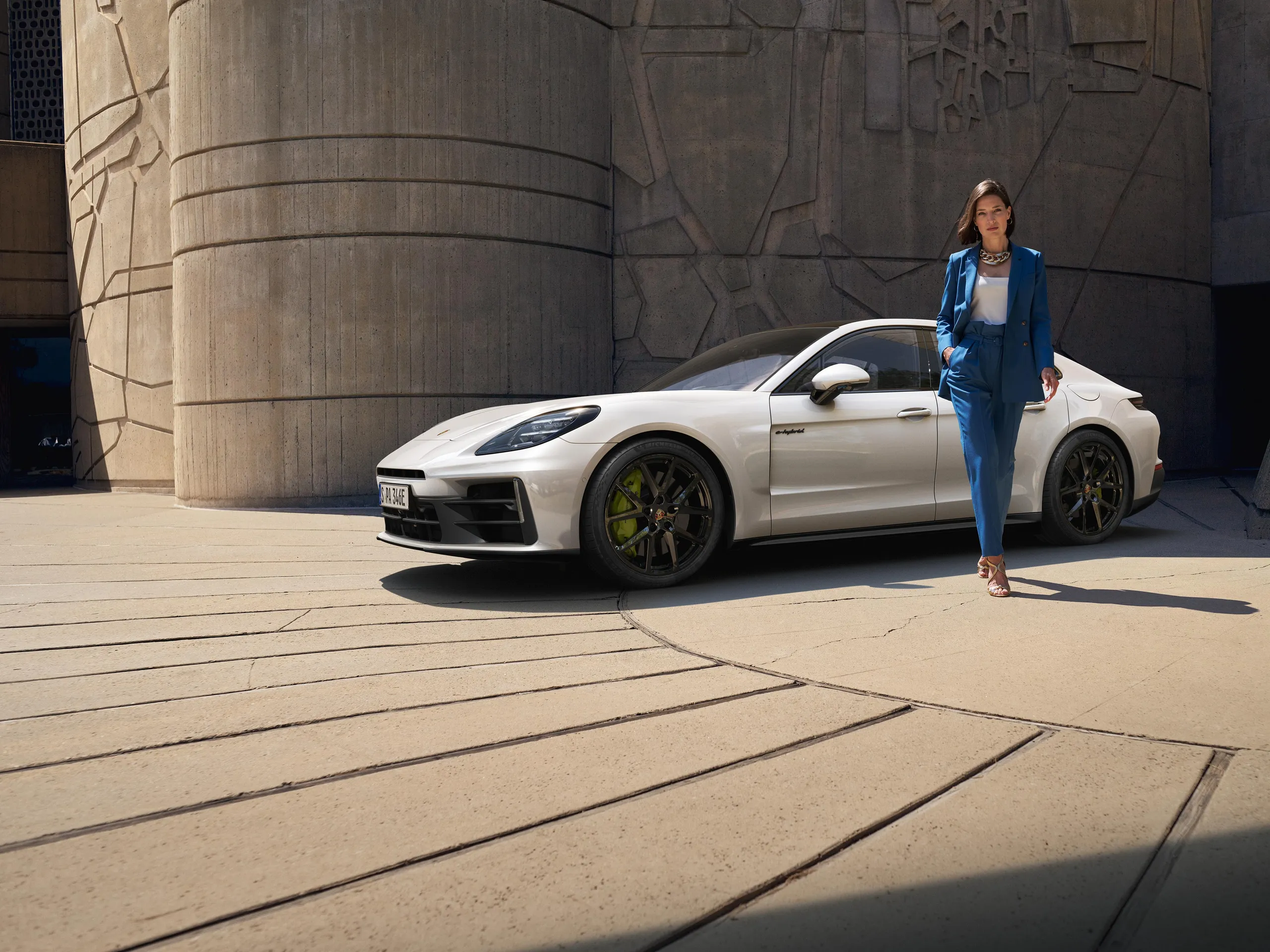 Side shot of a white Panamera 4 E-Hybrid standing in front of a modern building with a woman standing next to it.