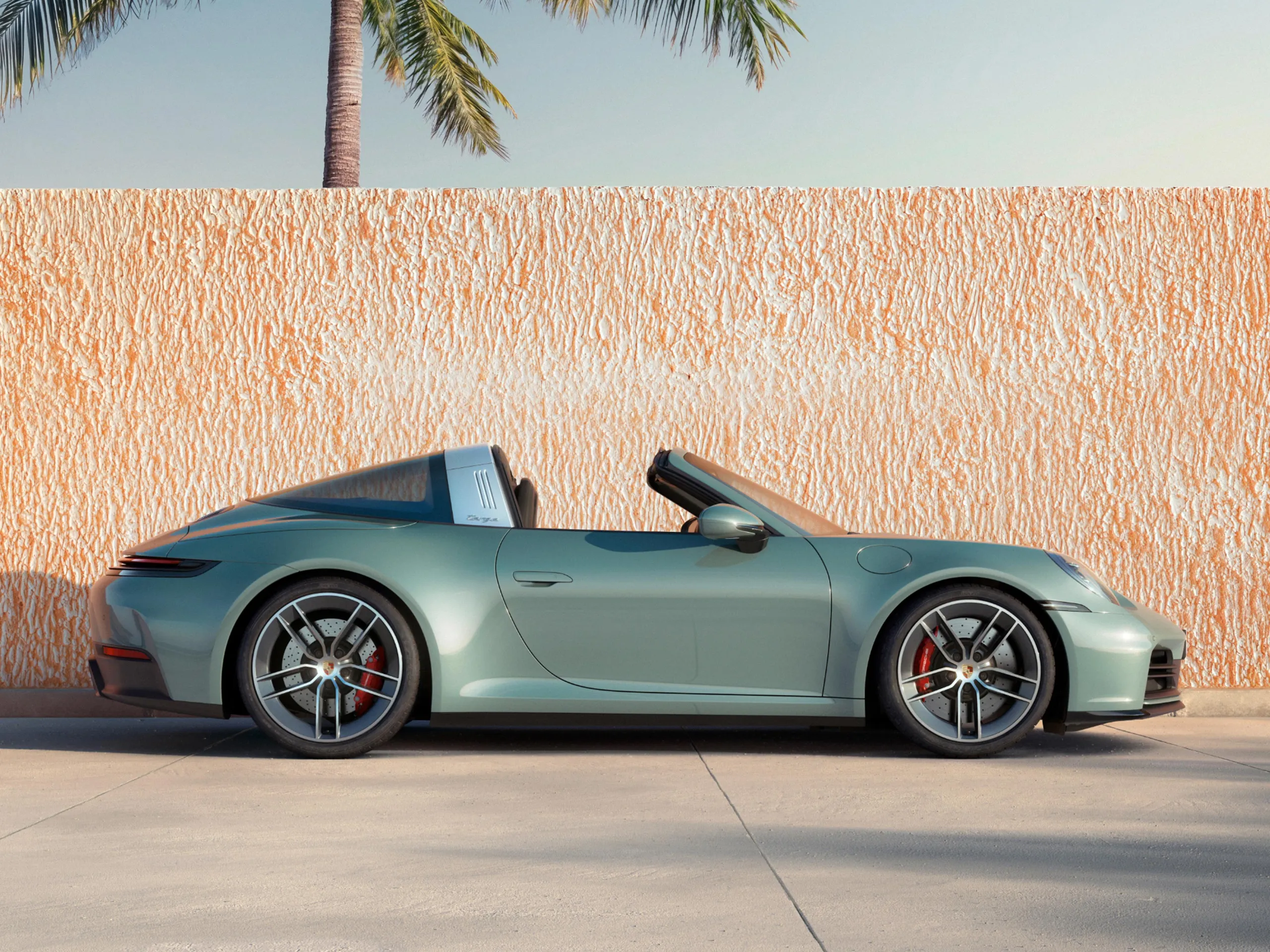 Side shot of shade green metallic 911 Targa 4S in front of orange low wall.