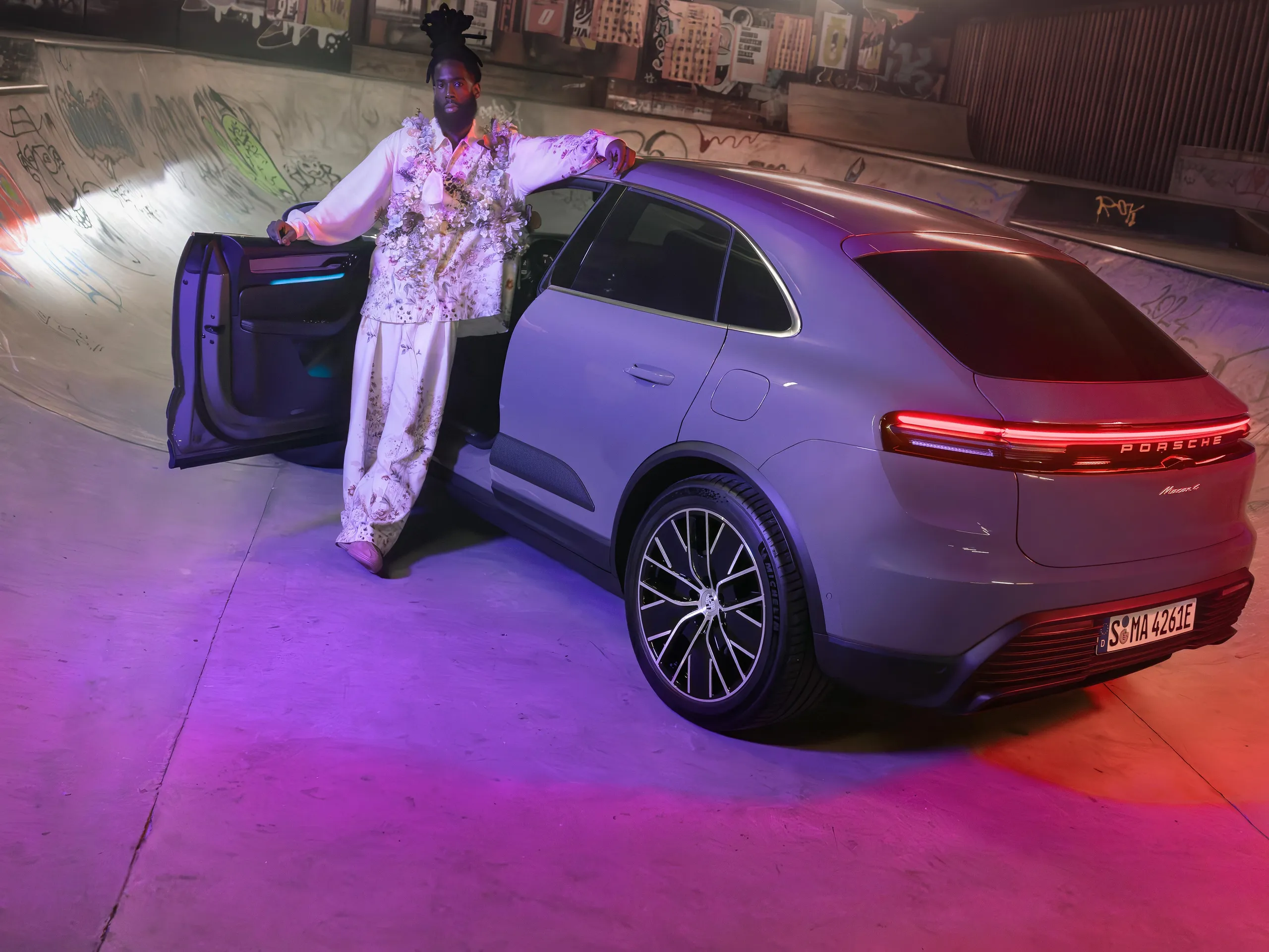 An all-electric Macan in an urban skateboard park with a man standing by the open driver's door.