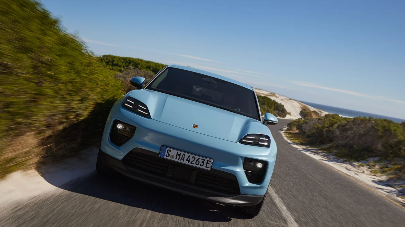 Several dynamic shots of a Frozen Blue Metallic Macan Electric driving on a road by the beach.