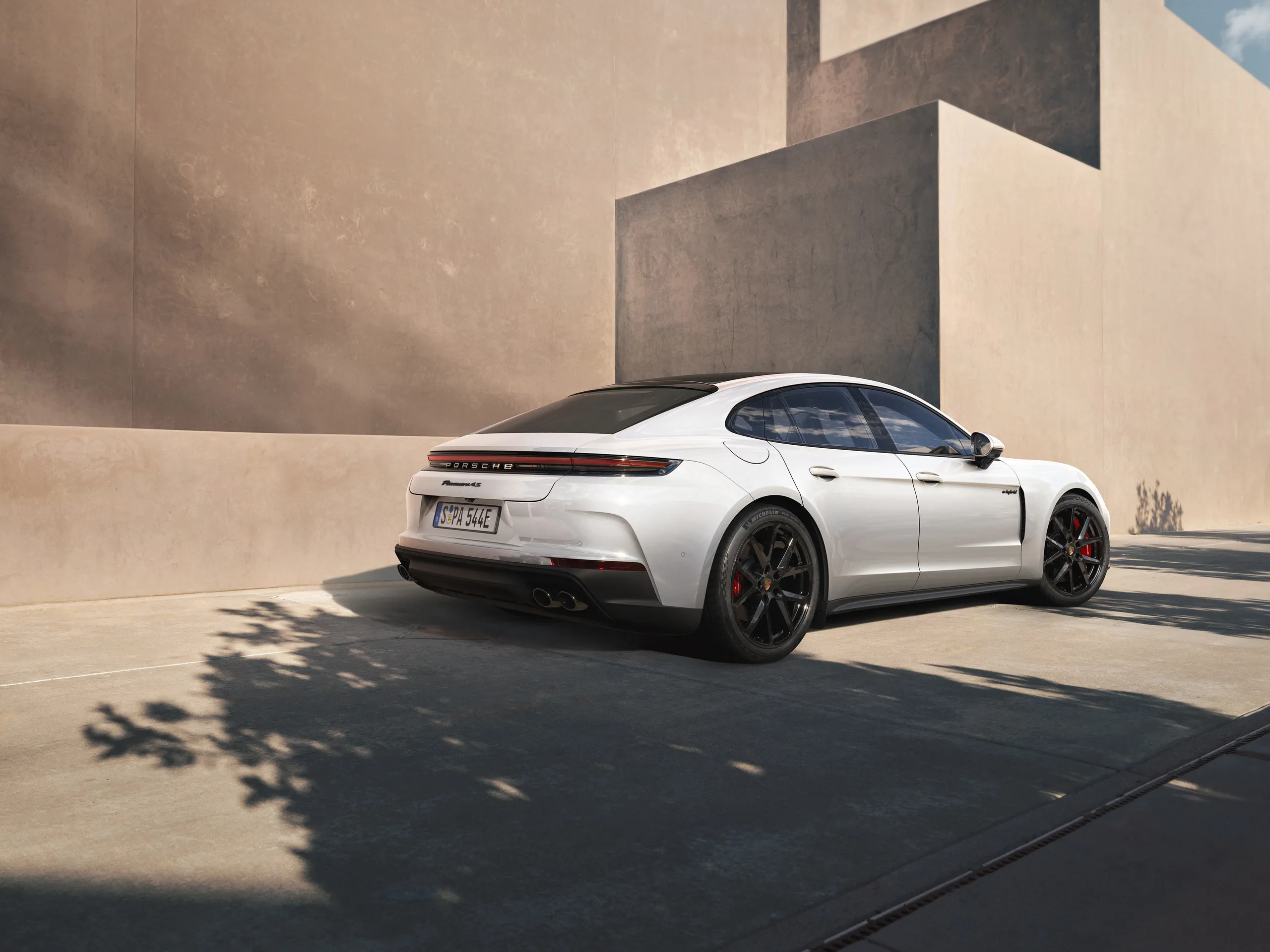 Rear shot of a white Panamera 4S E-Hybrid standing on the road in front of a modern building.