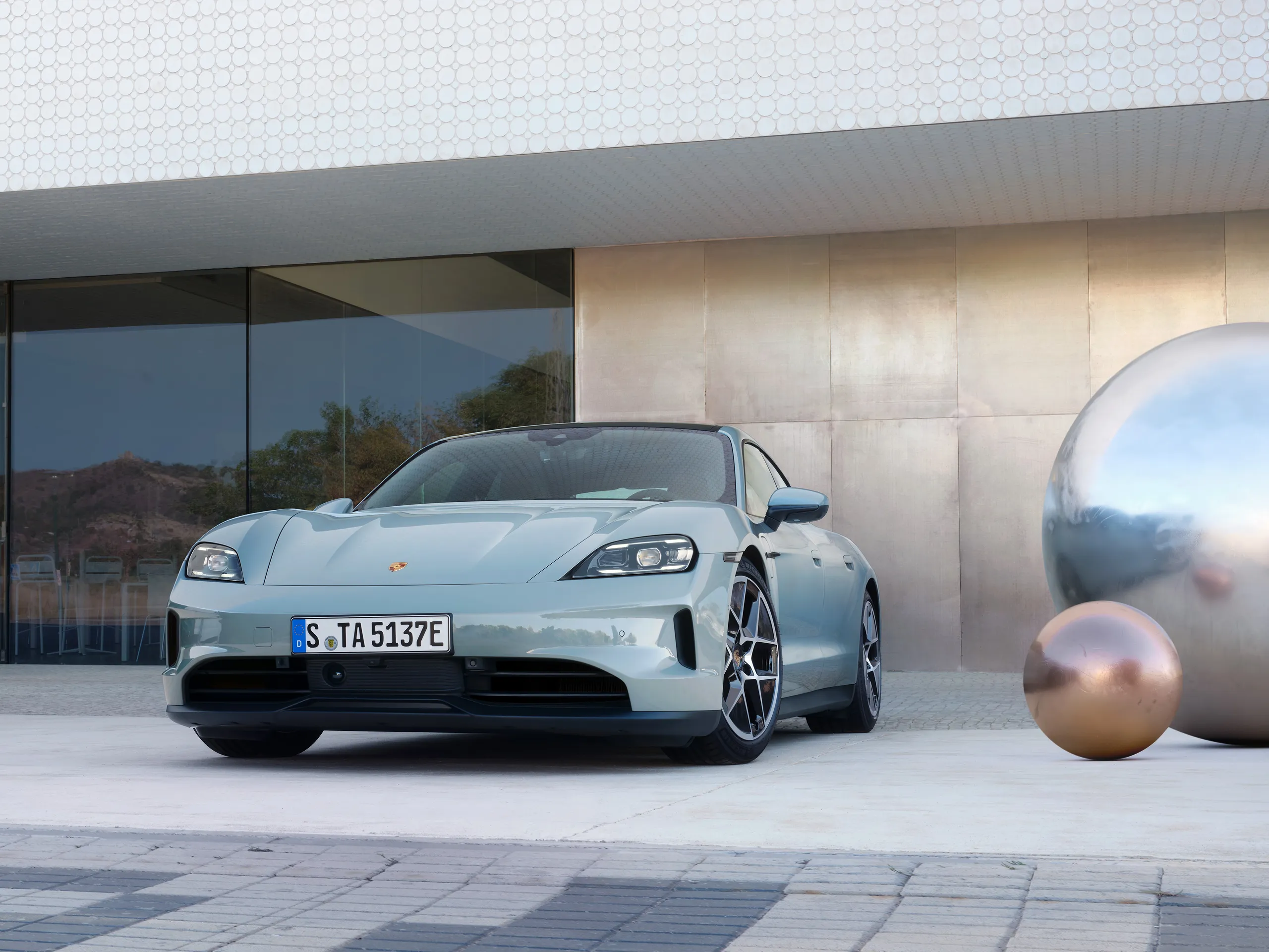 Front shot of a shadegreen metallic Taycan parked inrfront of a modern building.