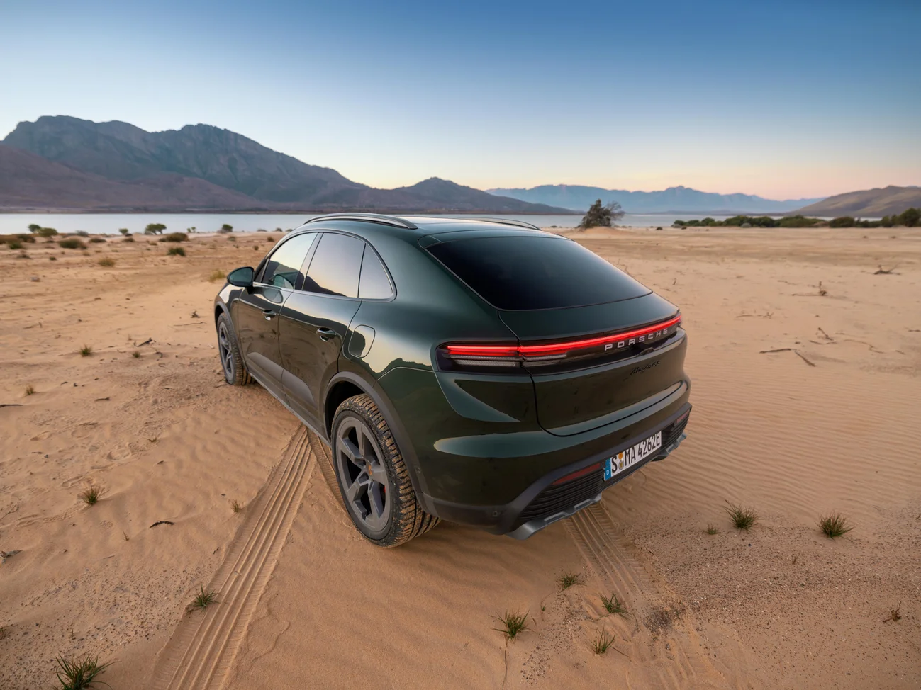 Rear shot of an Oak Green Metallic Neo Macan 4S standing in front of a lake with the mountains in the background.