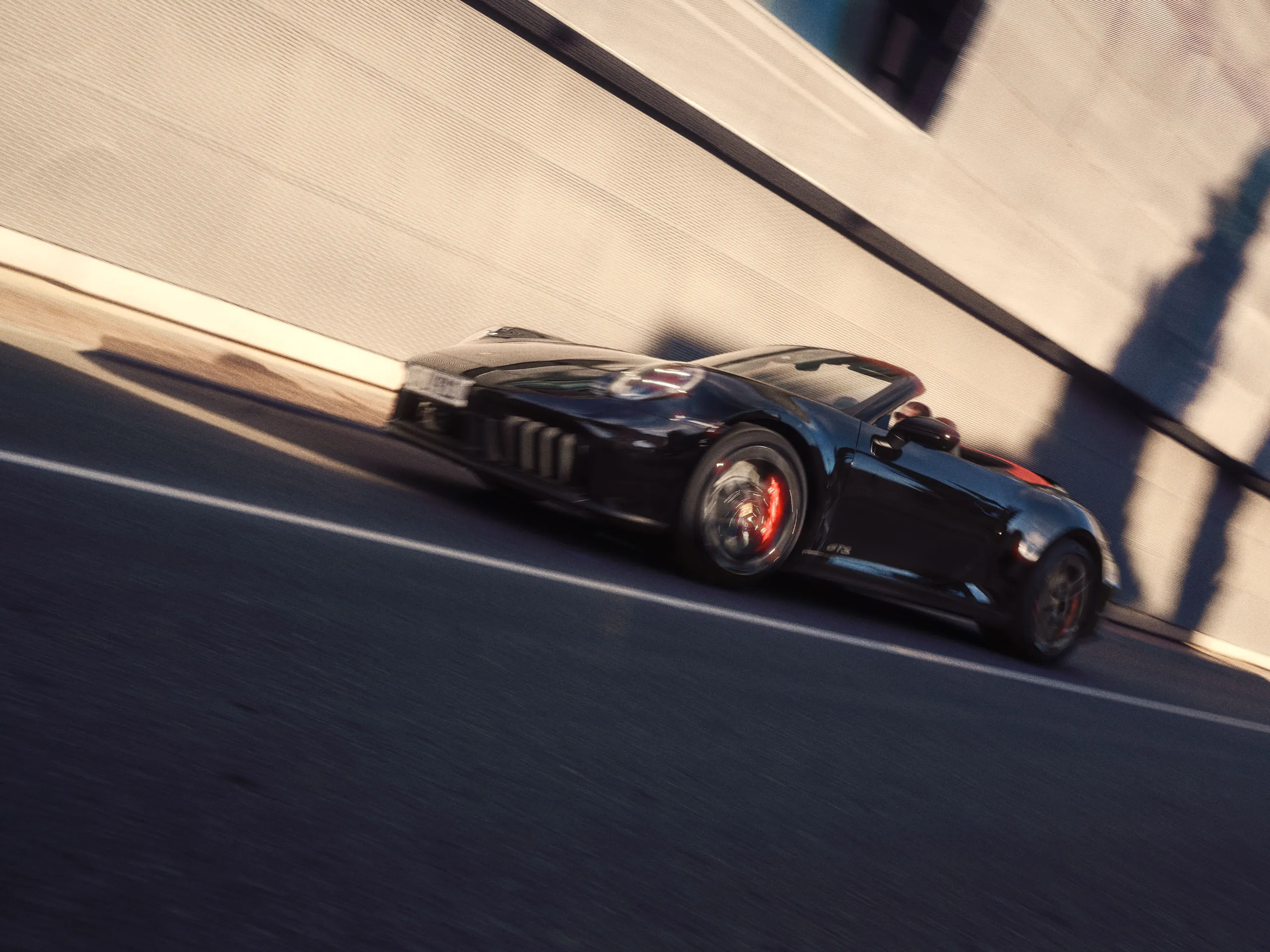 Side shot of a Jet Black Metallic 911 Carrera GTS Cabriolet driving on a road in front of a building.