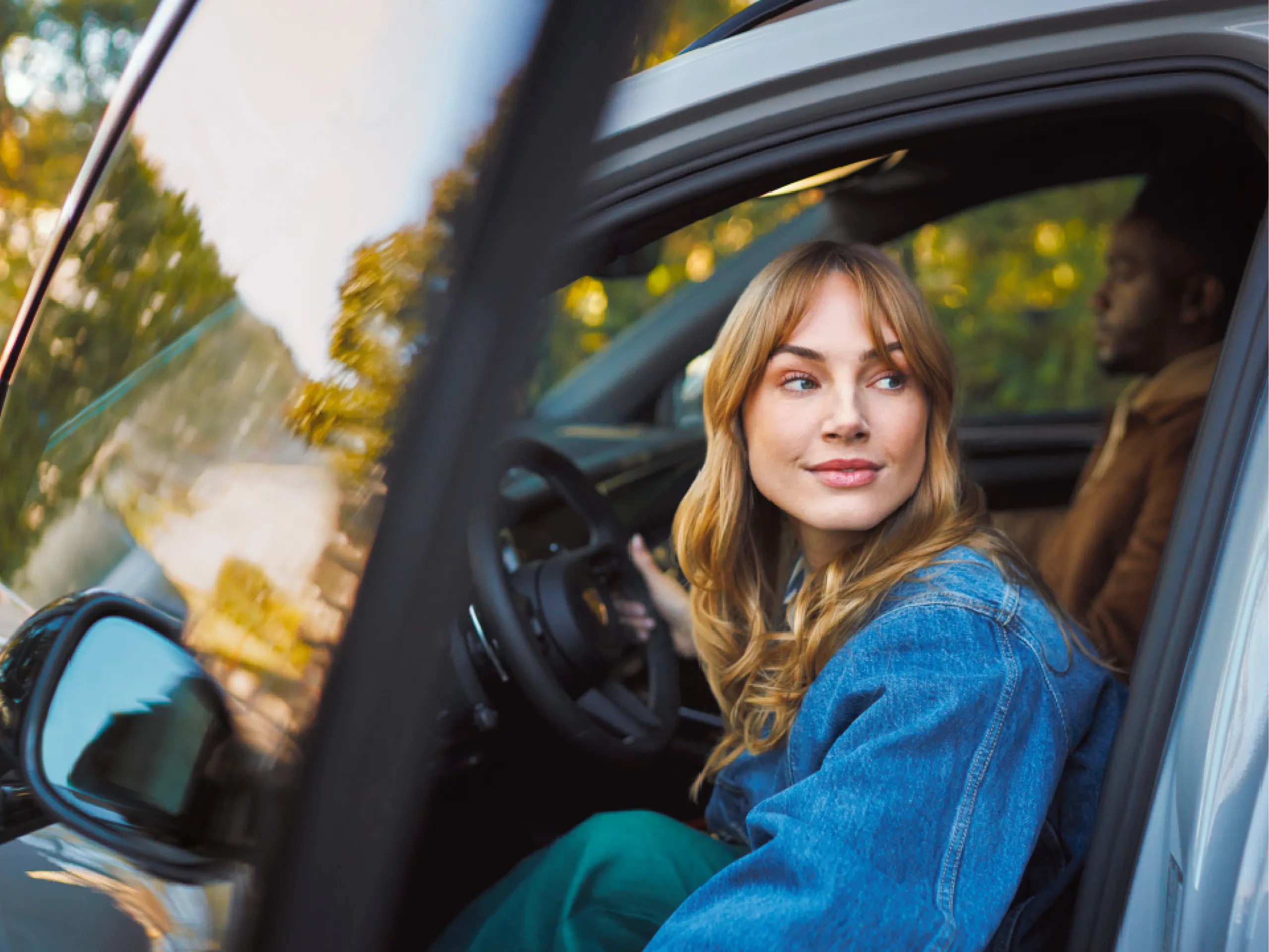 A woman sits in the driver's seat of a white SUV with the door open. She is softly smiling, looking away from the camera.