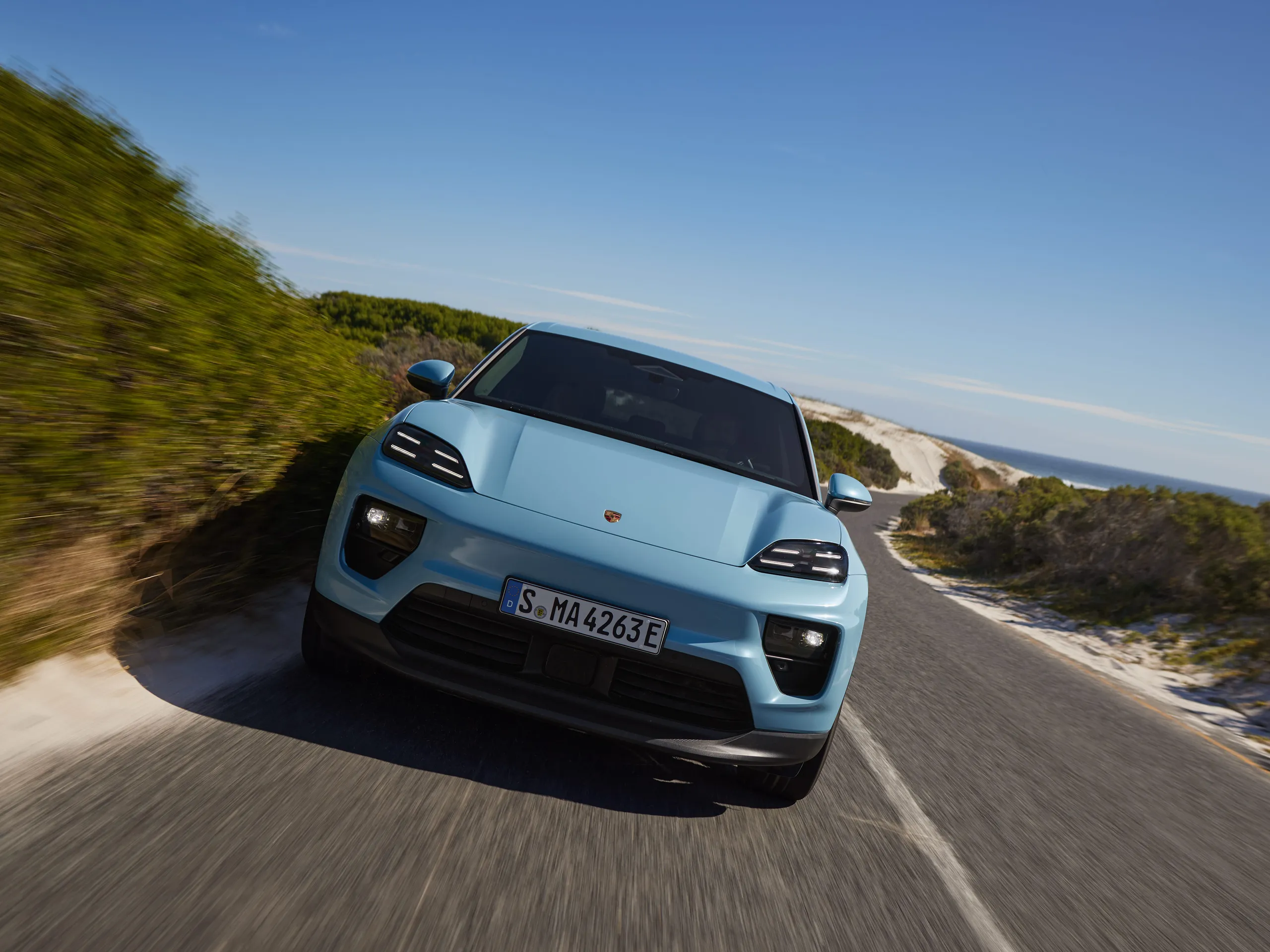 Front shot of a Frozen Blue Metallic Macan Electric driving on a road.