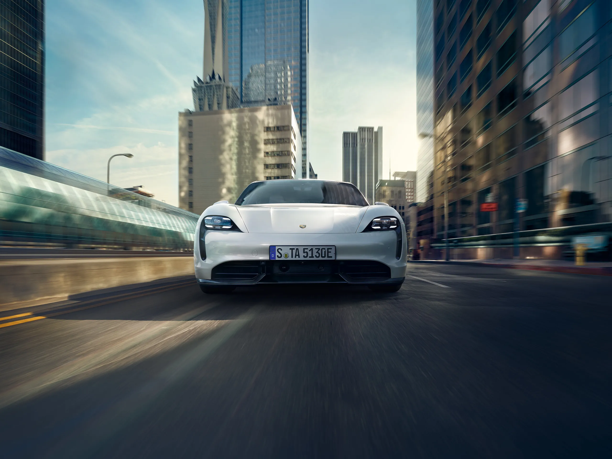 Front shot of a white Taycan Turbo S driving through an American city on a sunny day