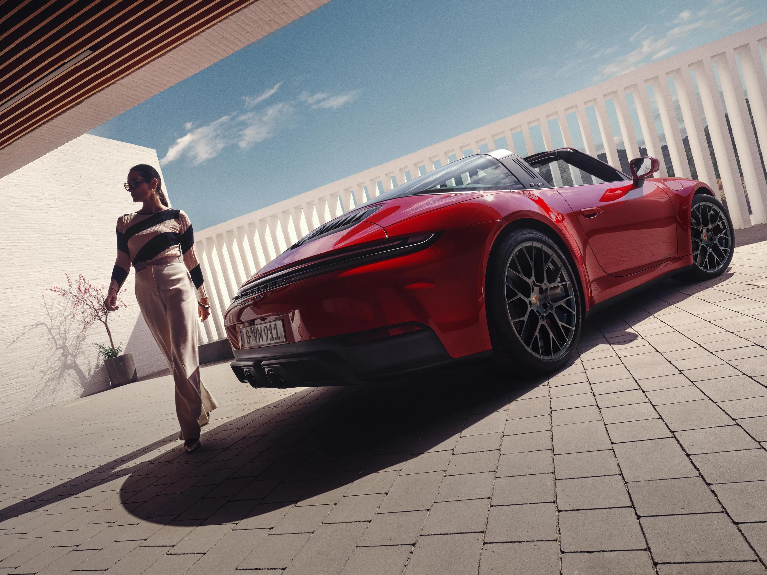 Rear shot of a Carmine Red 911 Targa 4 GTS with a woman standing next to it.