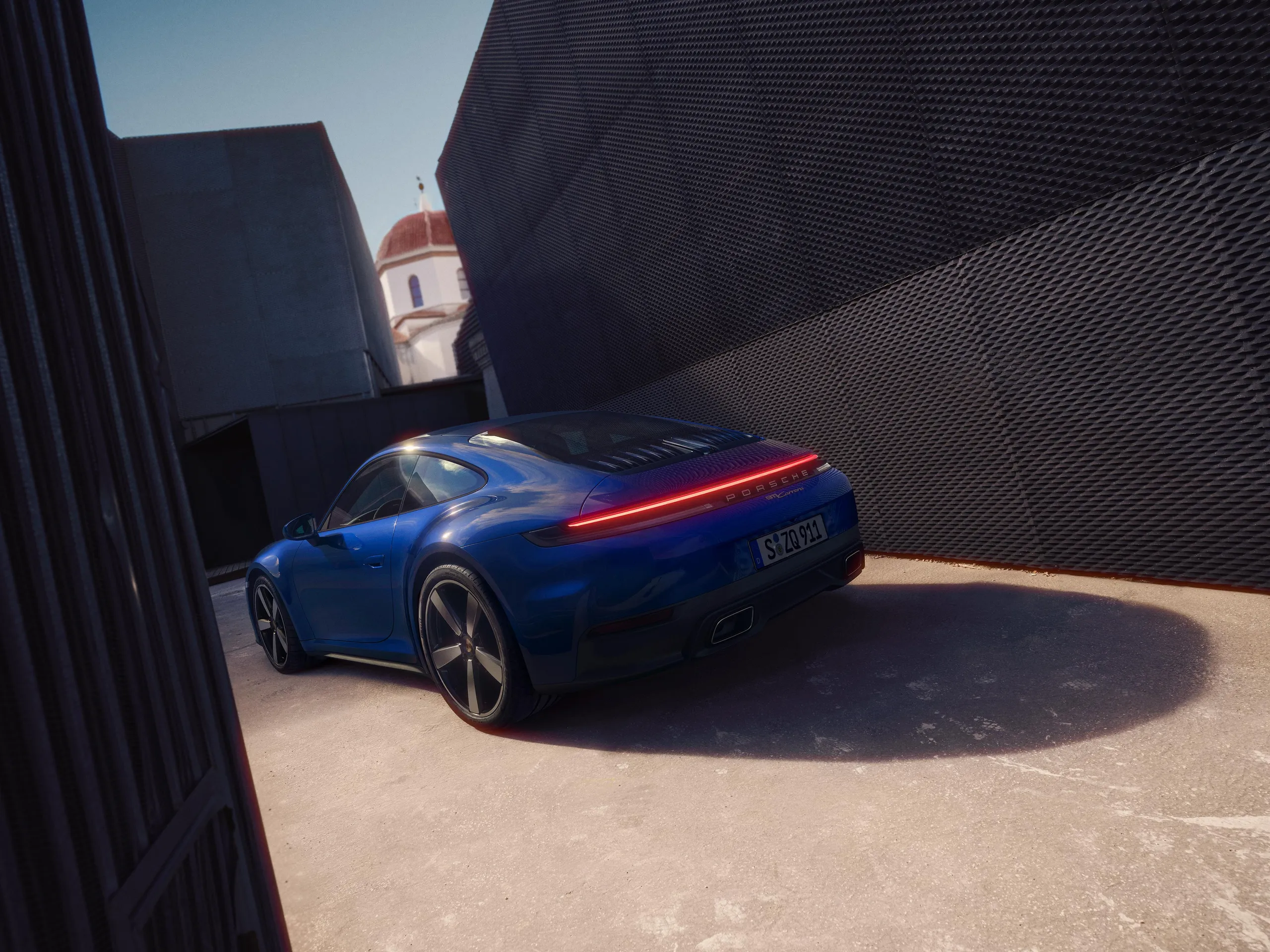Rear shot of a Luganoblue 911 Carrera standing on the road between modern buildings.