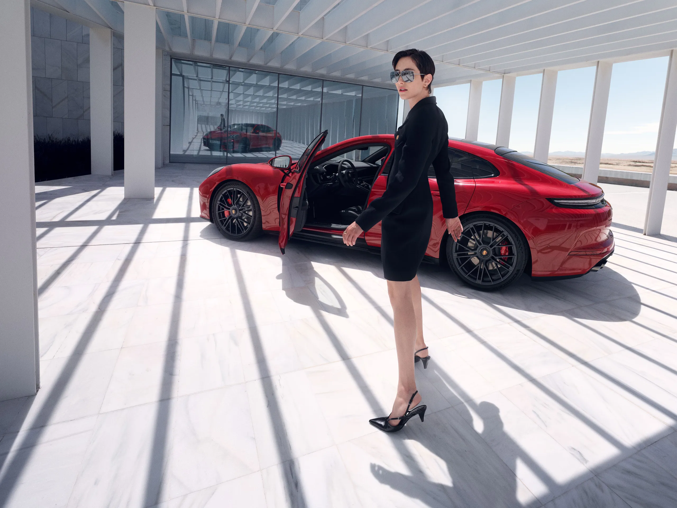 Side shot of a Carmine Red Panamera GTS standing in front of a modern building with a woman standing next to it.