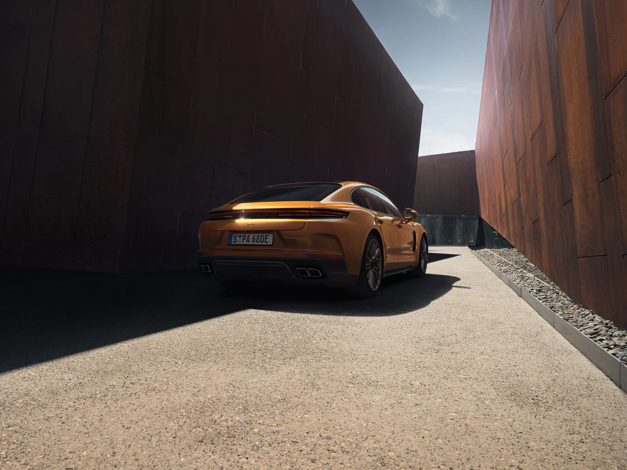 Rear shot of the new Panamera Turbo E-Hybrid in Madeira Gold Metallic standing on the road between modern buildings.