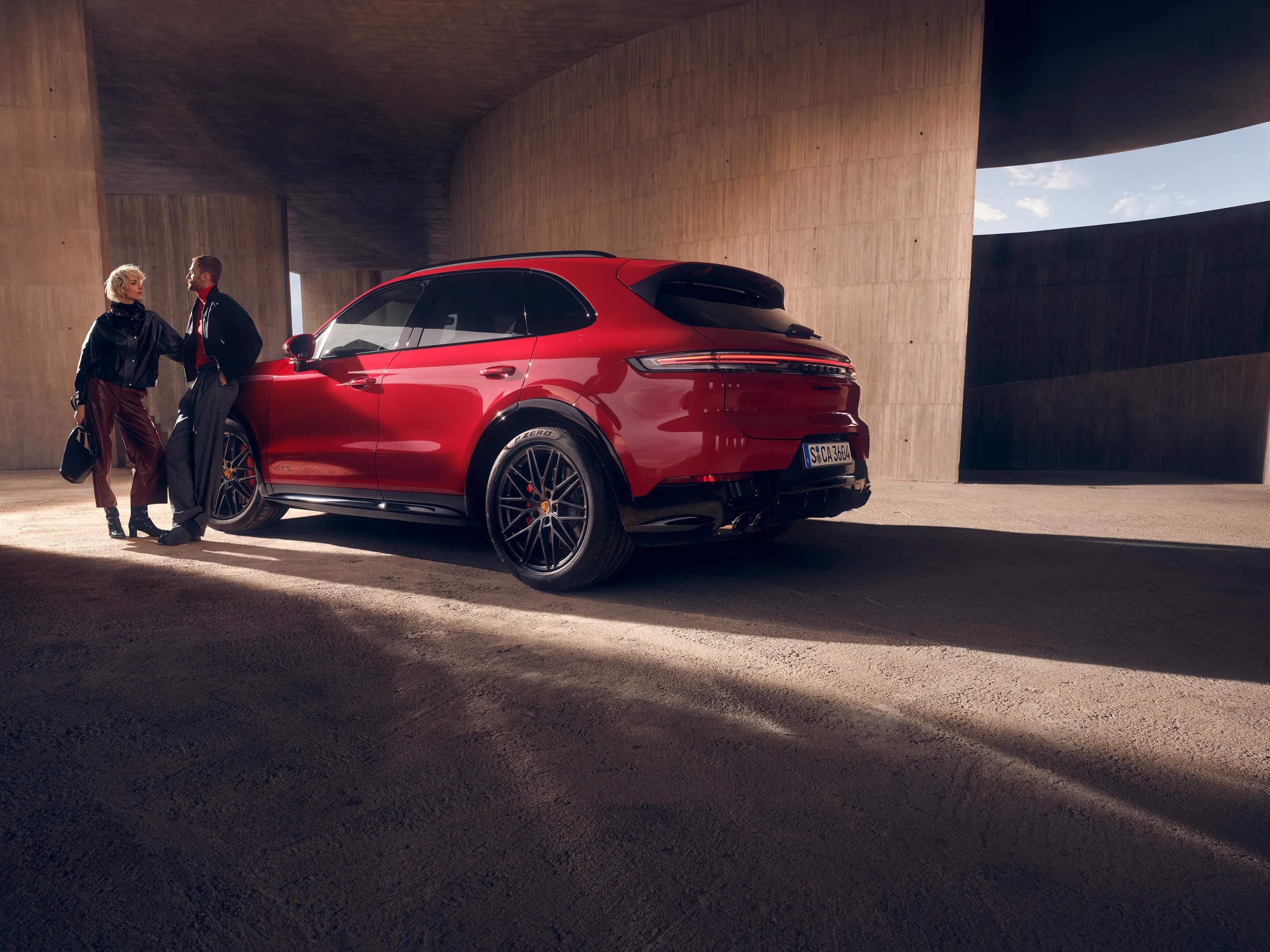 A man and a women stand in front of a red Cayenne GTS.
