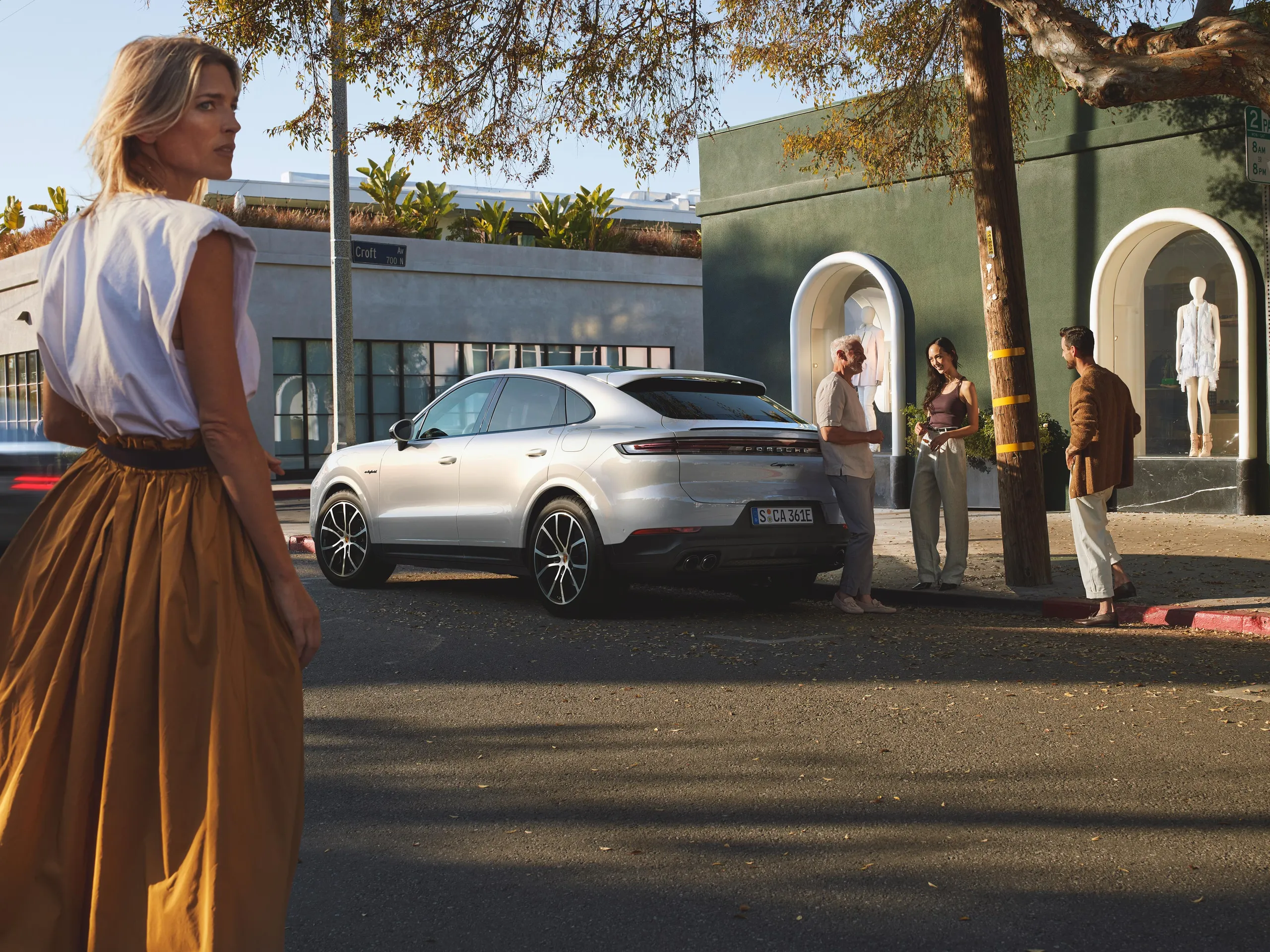 A group of people stand in front of the rear of a white Cayenne E-Hybrid Coupé on the side of the road in a city.