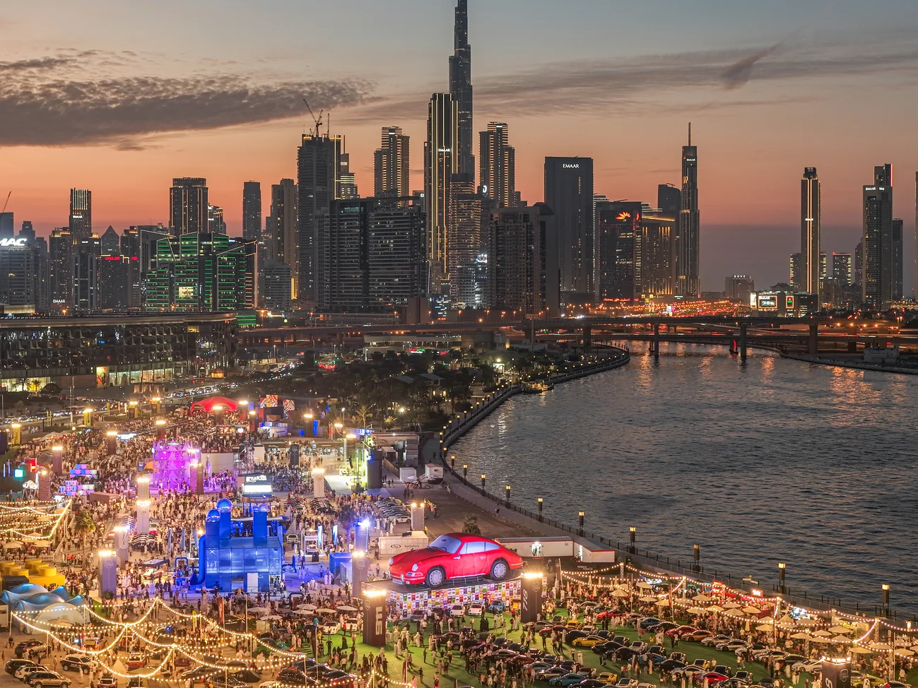 A drone shot of the Porsche event with thousands of attendees and cars, Burj Khalifa in the background, showcasing the scale